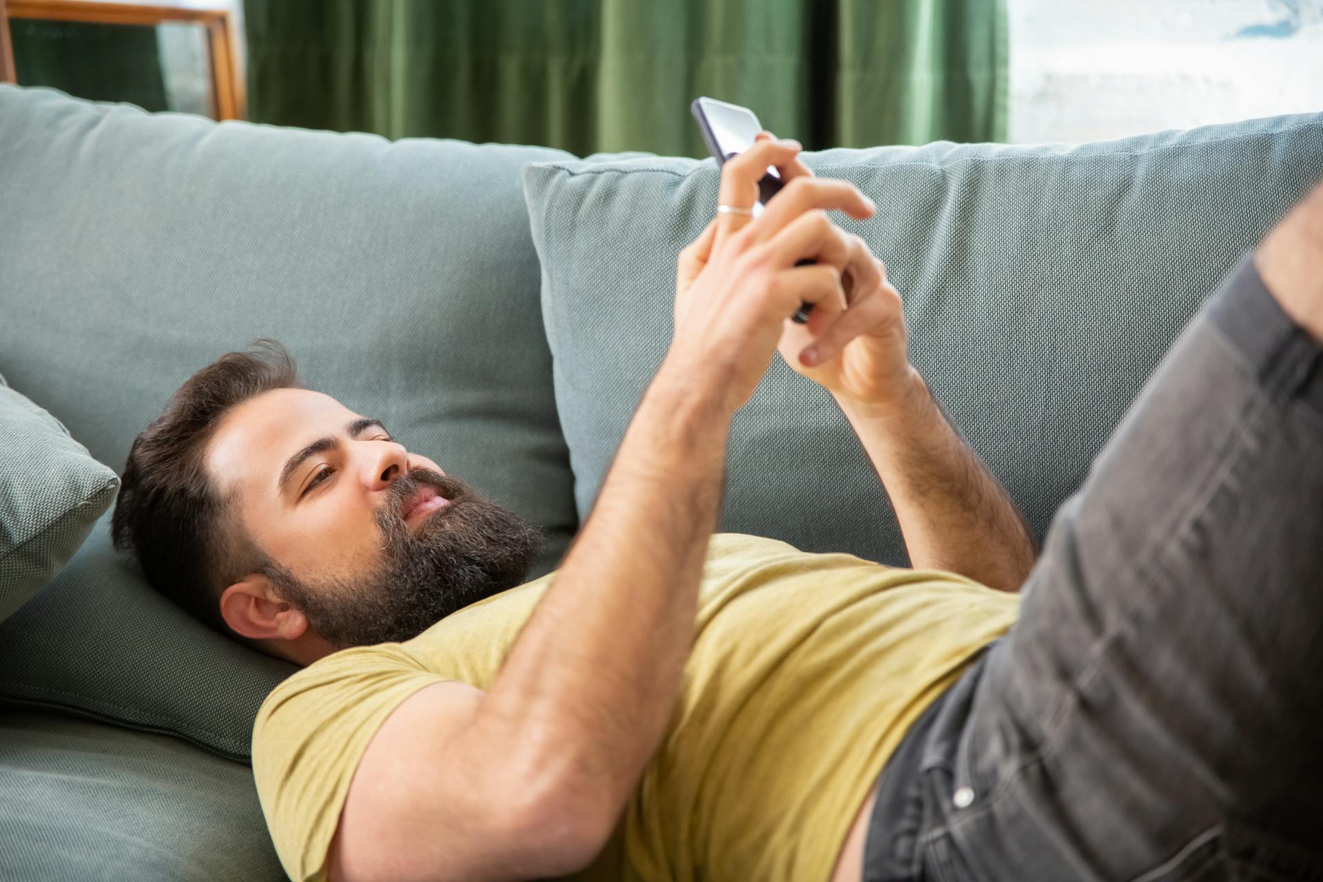 Un homme utilisant son téléphone alors qu'il est allongé sur le canapé | Source : Pexels