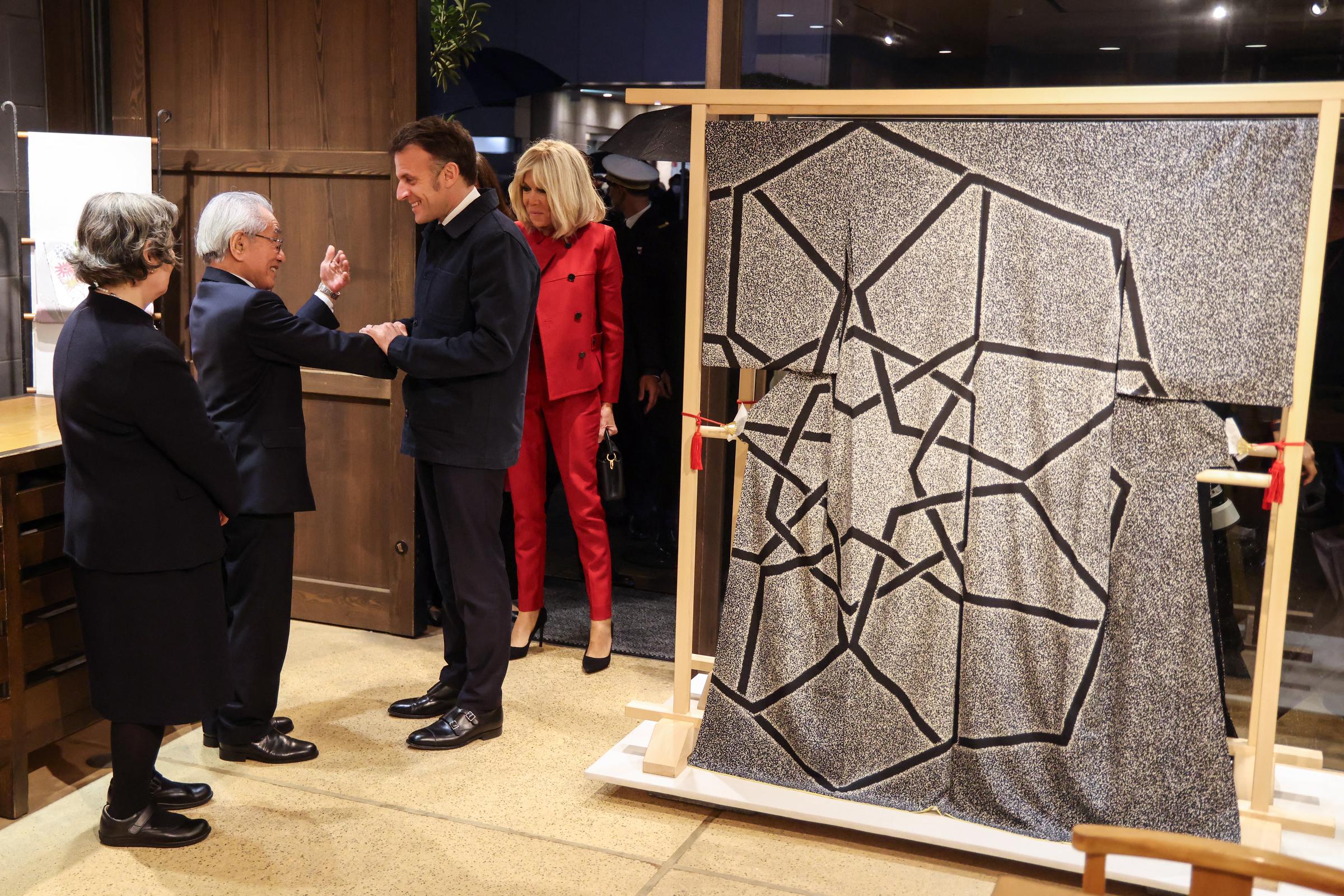 Le président français Emmanuel Macron (au centre) et son épouse Brigitte Macron (à droite) sont accueillis par l'artiste textile japonais Kunihiko Moriguchi (2e à gauche) au showroom Ginza Motoji à Tokyo, le 31 mars 2026 I Source : Getty Images
