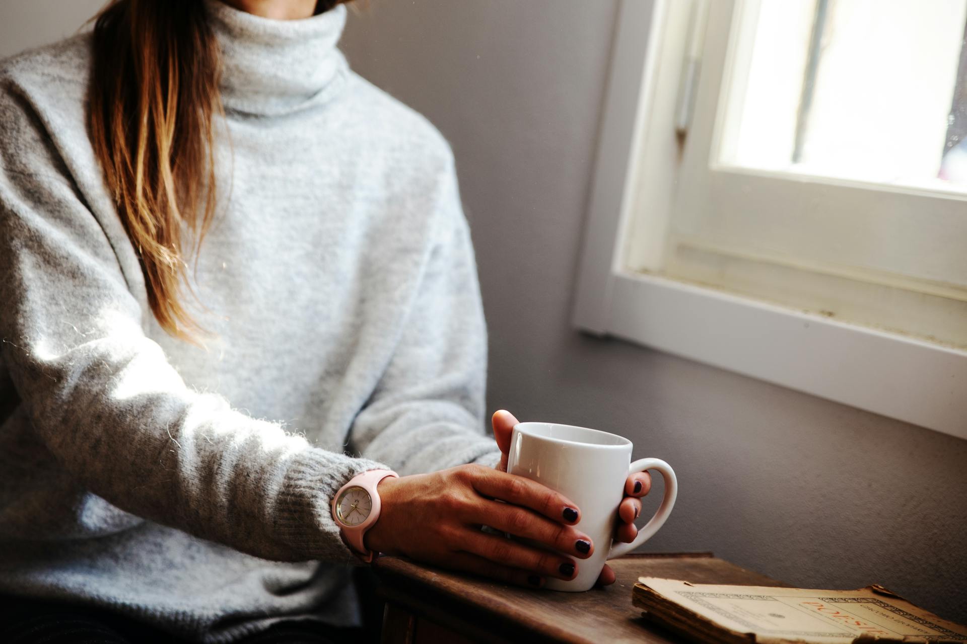 Une femme tenant une tasse à café, assise près d'une fenêtre | Source : Pexels