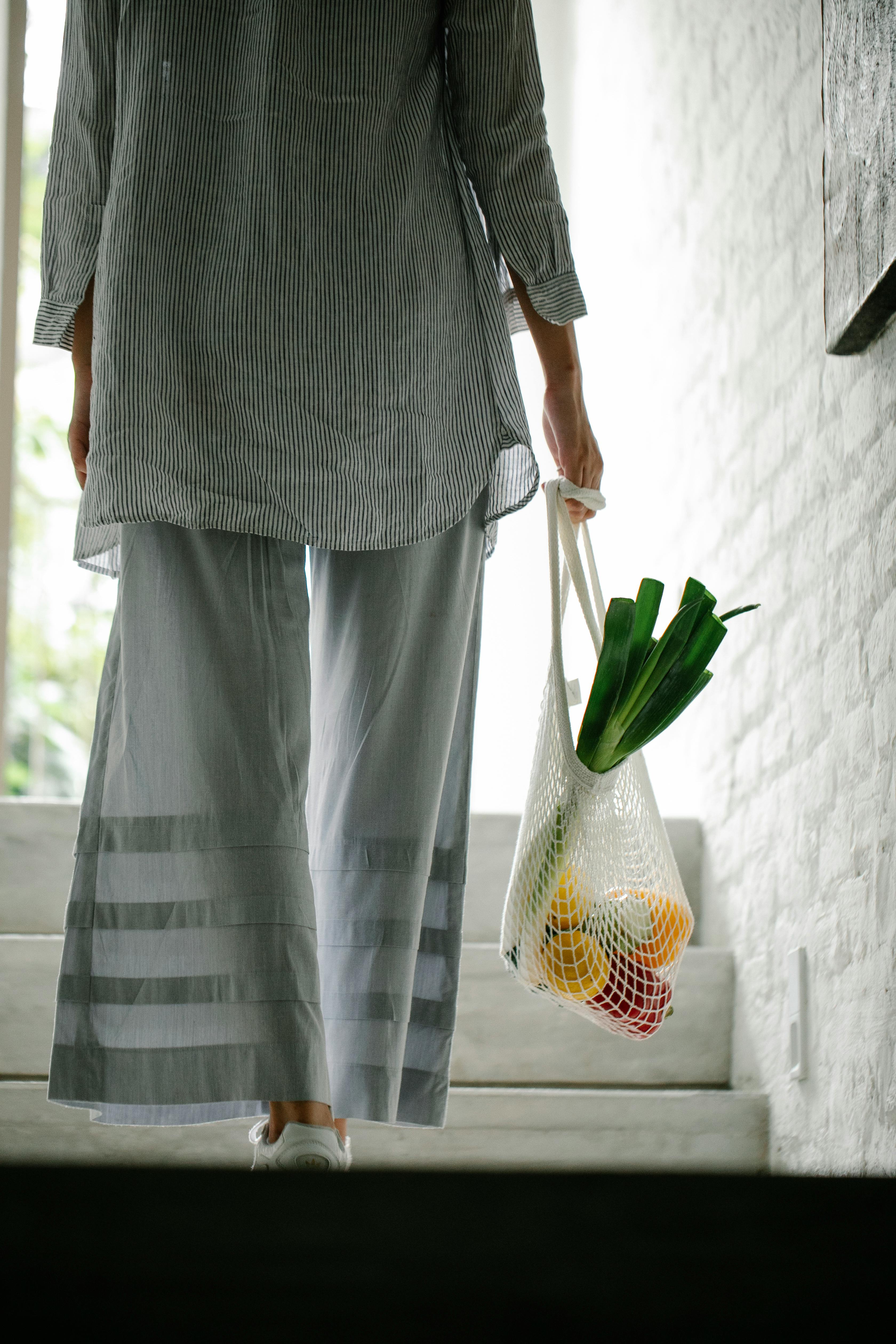 Une femme transportant des légumes dans un sac dans l'escalier d'une maison | Source : Pexels