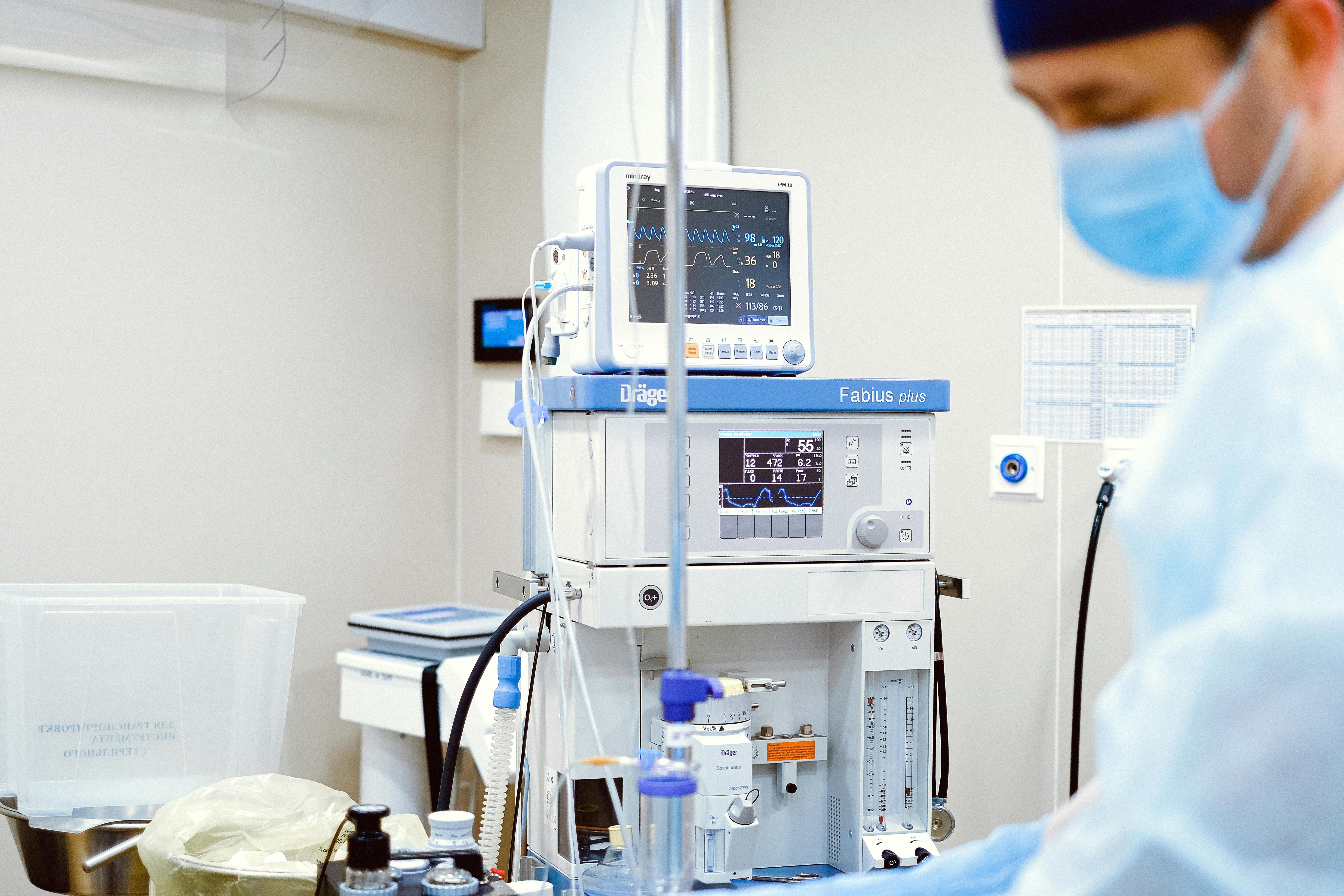 Un médecin portant un masque se tient à côté de divers appareils de surveillance médicale. | Source : Pexels