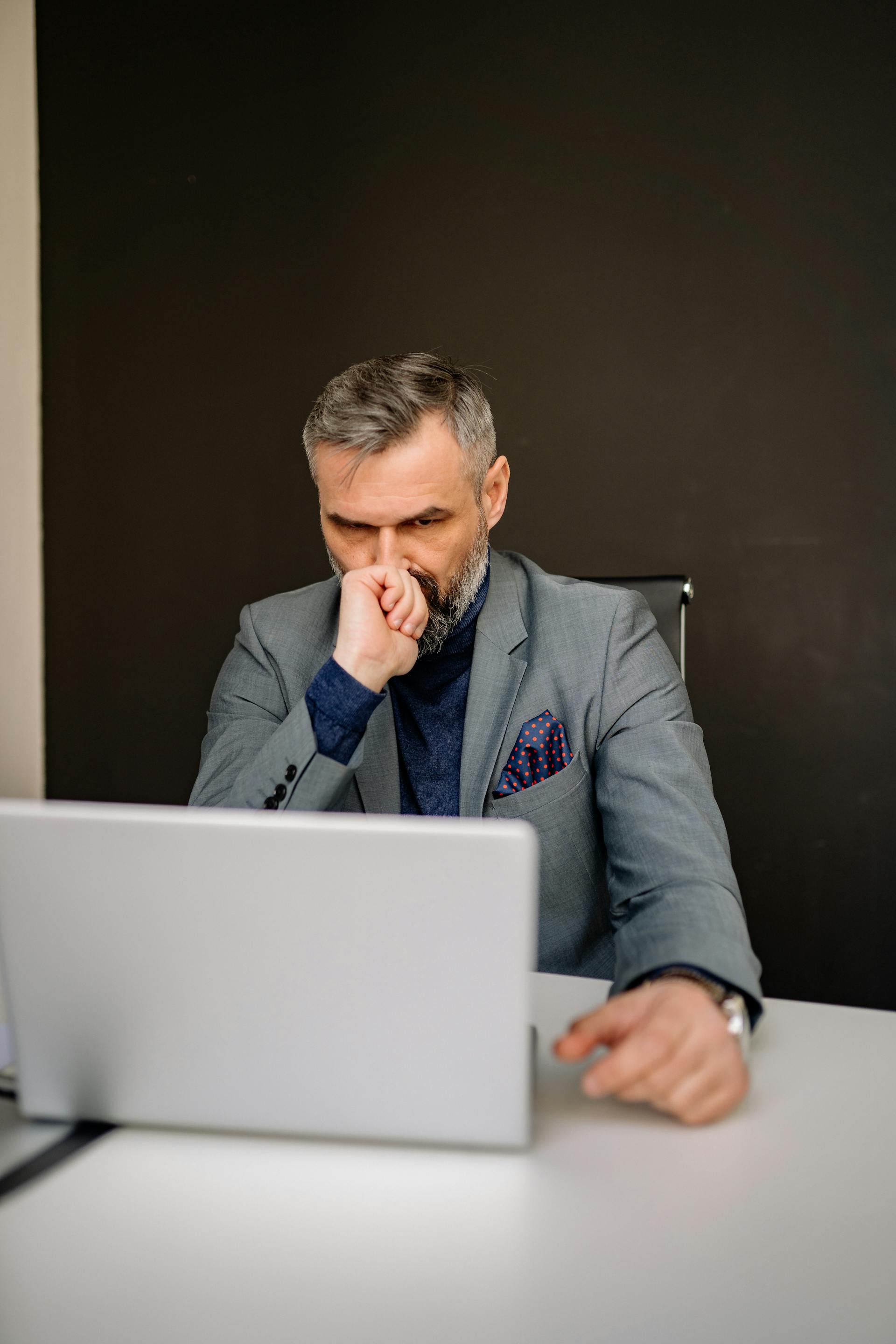 Un homme regarde son ordinateur portable alors qu'il est assis au bureau | Source : Pexels