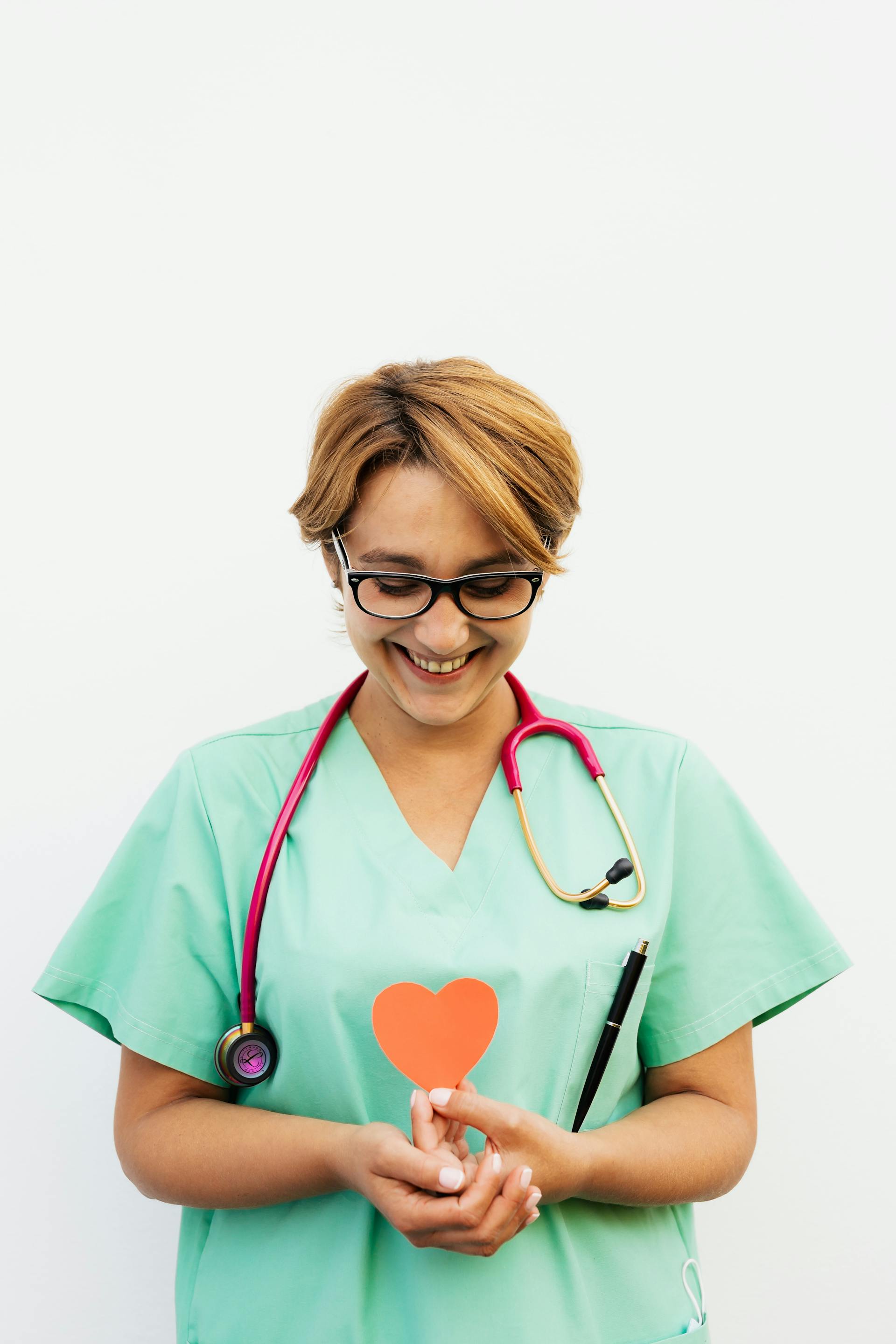 Une infirmière souriante tenant un cœur en papier rouge | Source : Pexels