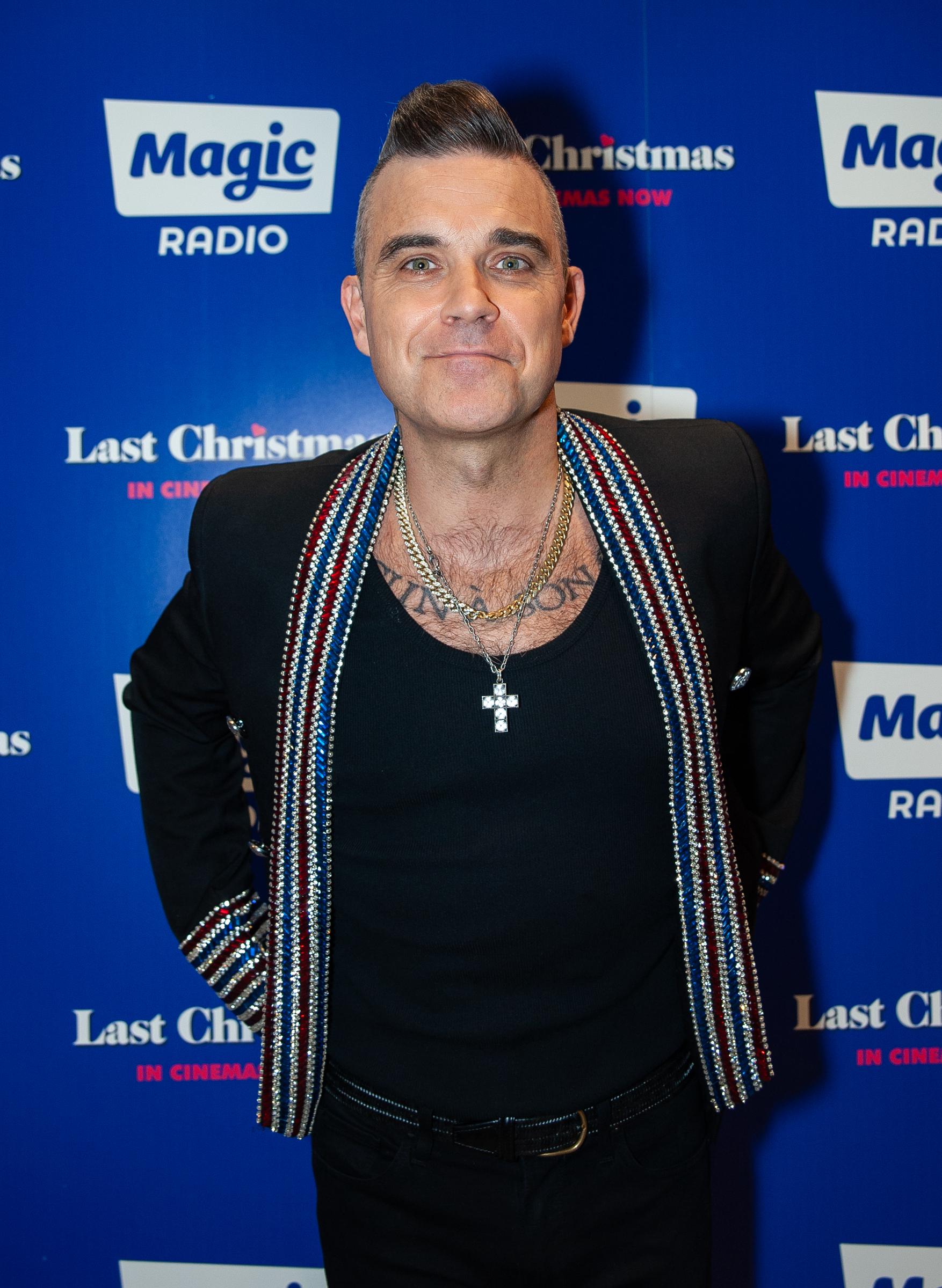 Robbie Williams participe à l'émission Magic of Christmas de Magic Radio avec « Last Christmas » le 24 novembre 2019 à Londres, en Angleterre. Vêtu d'une veste à paillettes et de chaînes superposées, il prend une pose assurée, apportant son charme caractéristique à cet événement festif.