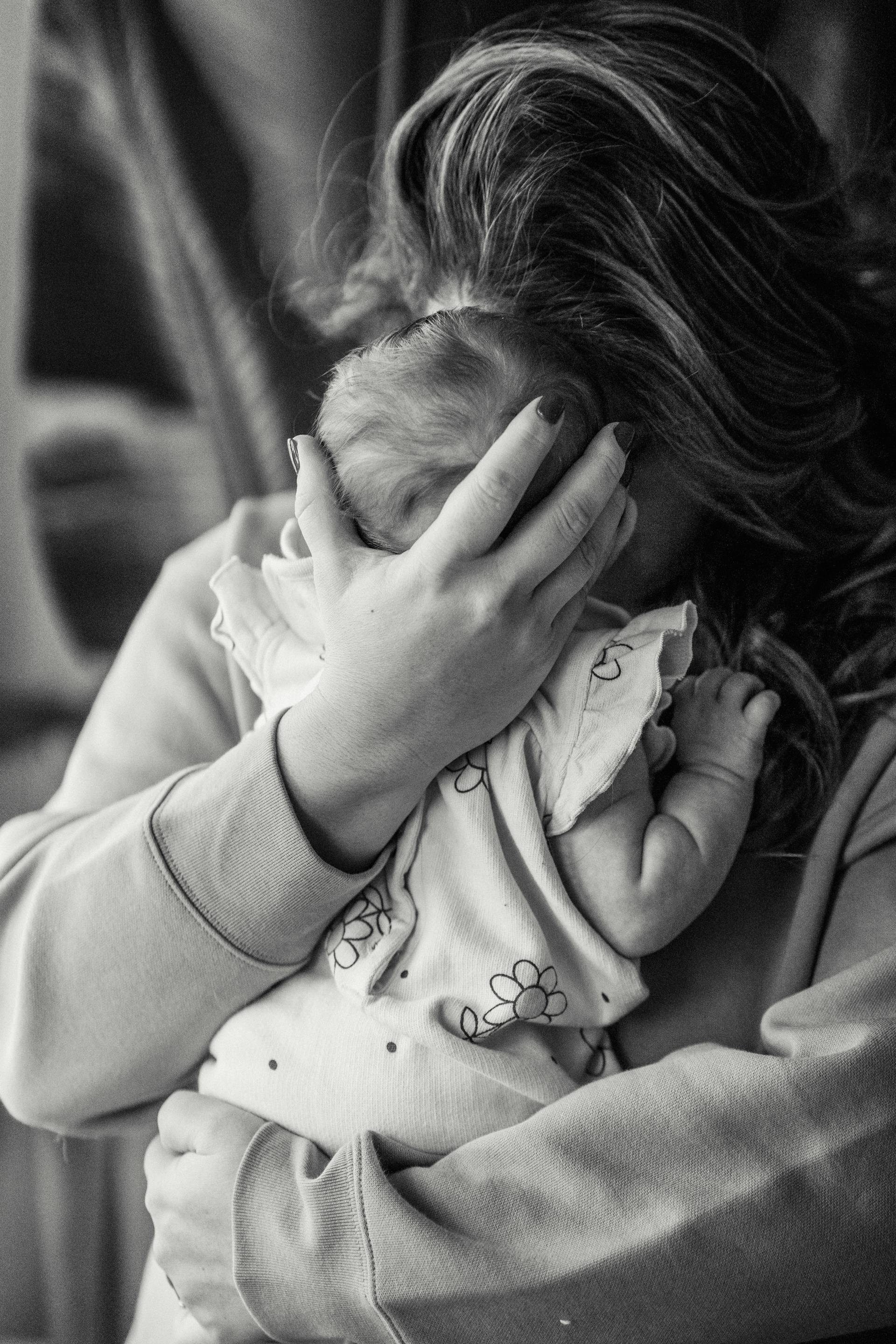 Photo en niveaux de gris d'une femme serrant son bébé dans ses bras | Source : Pexels