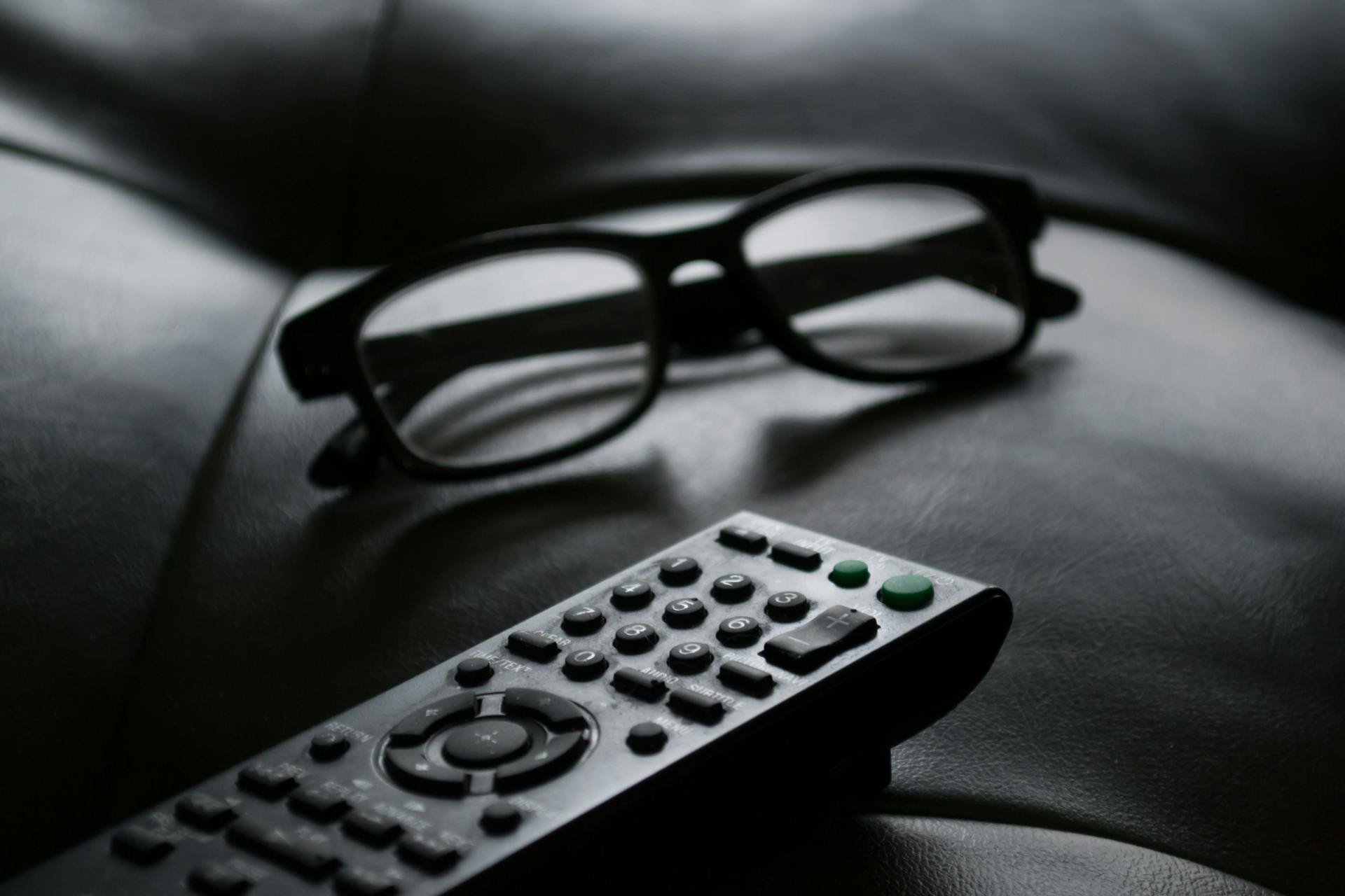 Photo en niveaux de gris d'une télécommande près de lunettes | Source : Pexels
