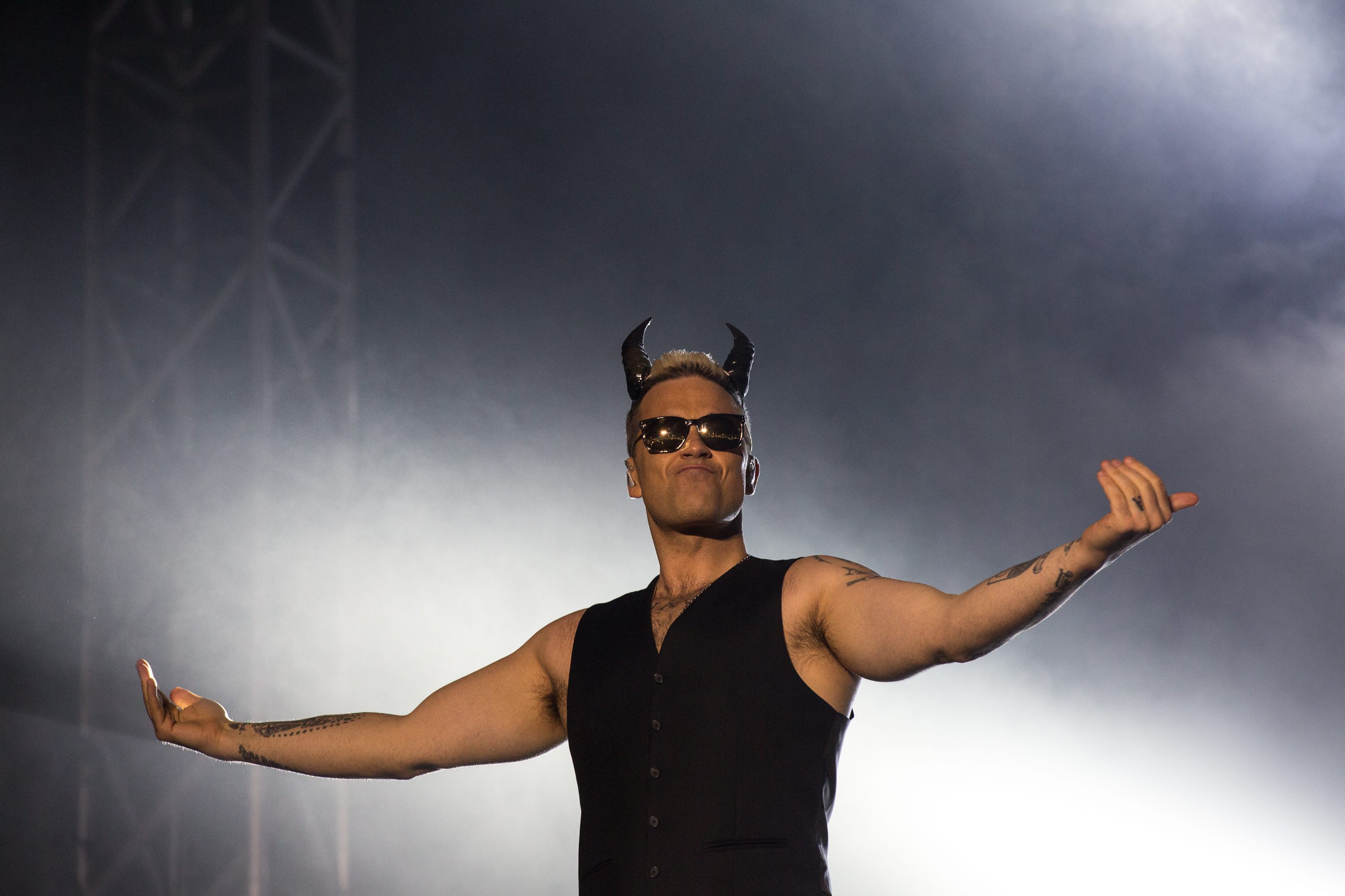 Robbie Williams au Hayarkon Park le 2 mai 2015, à Tel Aviv, en Israël. Vêtu de lunettes de soleil, d'un gilet sans manches et de cornes de diable, il a pris une pose théâtrale qui reflétait son sens du spectacle et son personnage ironique sur scène.