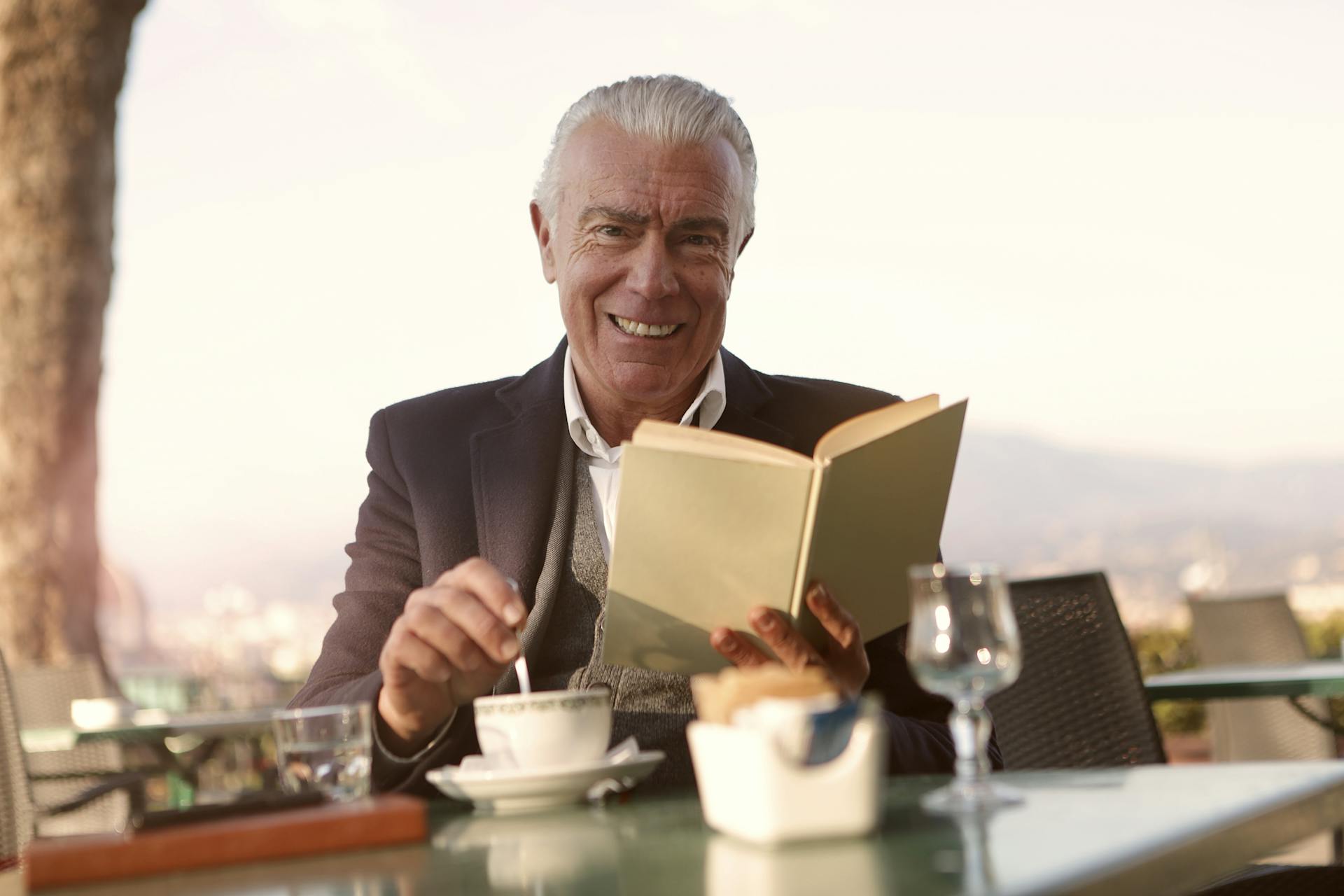 Un homme assis à une table et souriant tout en tenant un livre | Source : Pexels