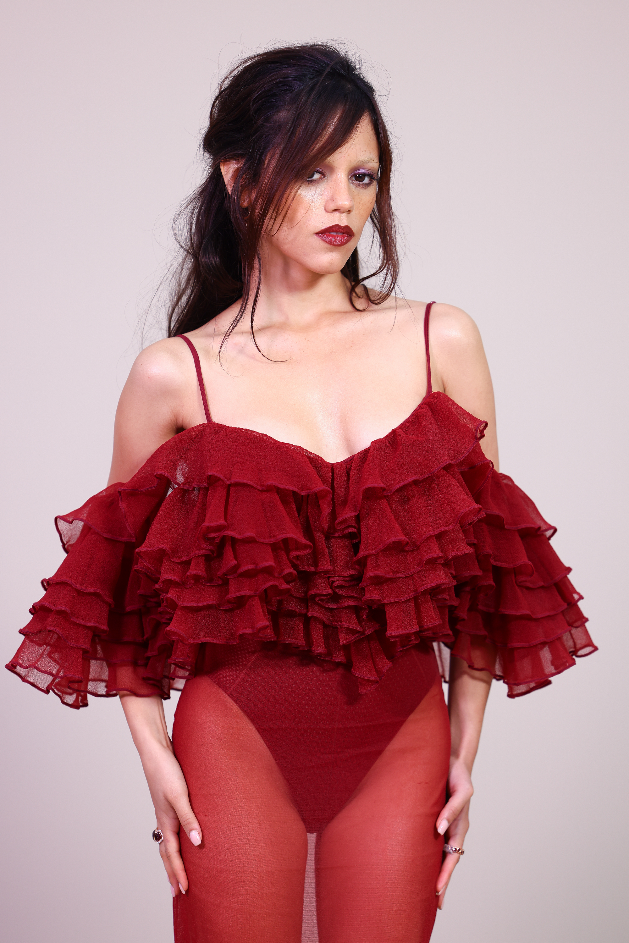 Jenna Ortega au défilé Givenchy Femme Printemps/Été 2026 lors de la Fashion Week de Paris, en France. Elle porte une robe rouge longue jusqu'au sol, avec un corsage à volants superposés et à bretelles spaghetti. Elle était assortie d'une jupe transparente superposée à une culotte taille haute.