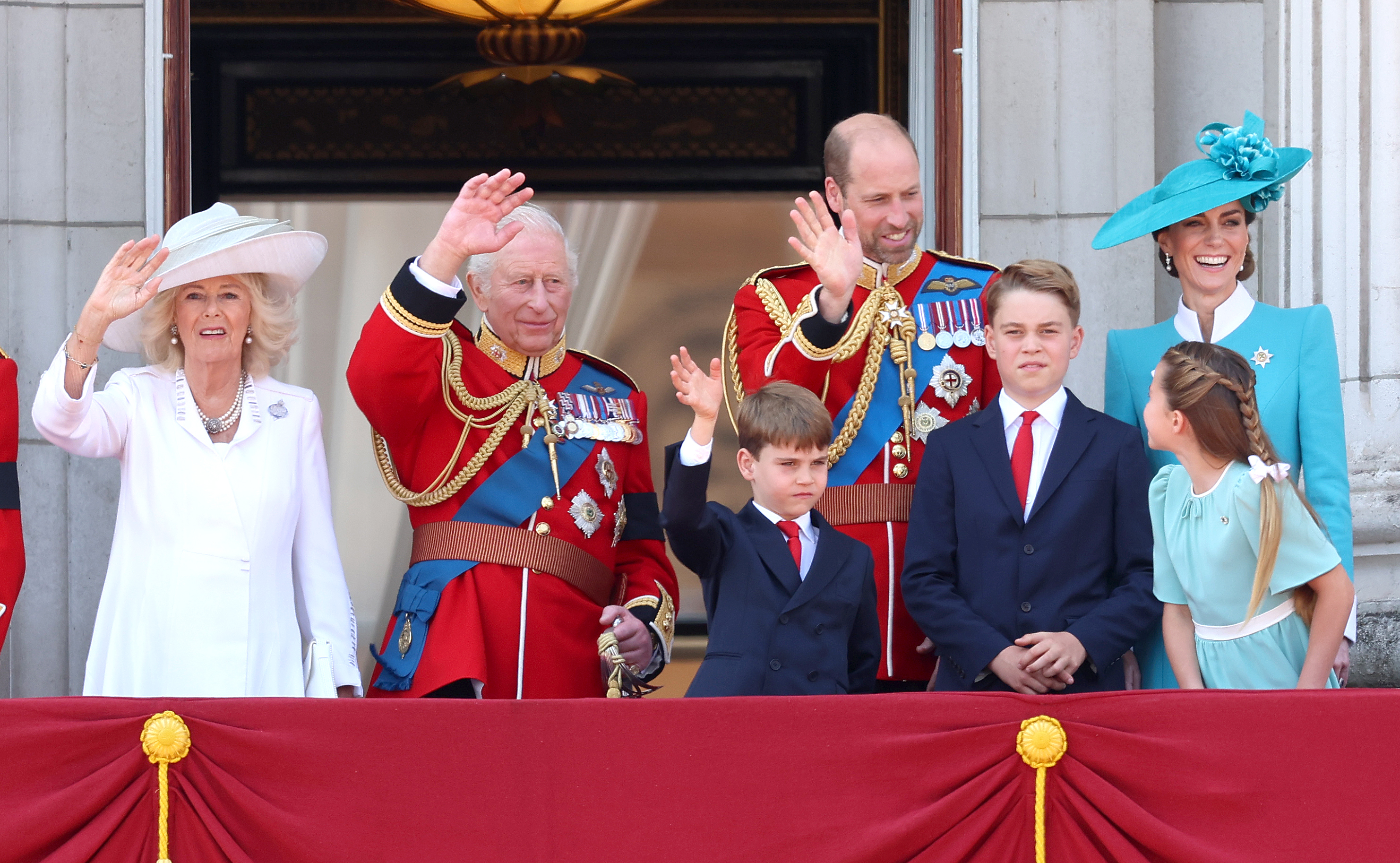 La reine Camilla, le roi Charles III et le prince et la princesse de Galles apparaissent au balcon du palais de Buckingham lors de la parade Trooping the Colour 2025, accompagnés de leurs enfants, le prince George, la princesse Charlotte et le prince Louis. Dans ce plan moyen, la princesse Catherine se distingue dans un blazer bleu sarcelle ajusté, doté de poignets blancs nets et d'un col blanc structuré. L'ensemble, visible dans ses moindres détails, reflète la sophistication royale tandis que la famille royale observe le spectacle militaire et salue la foule rassemblée en contrebas.