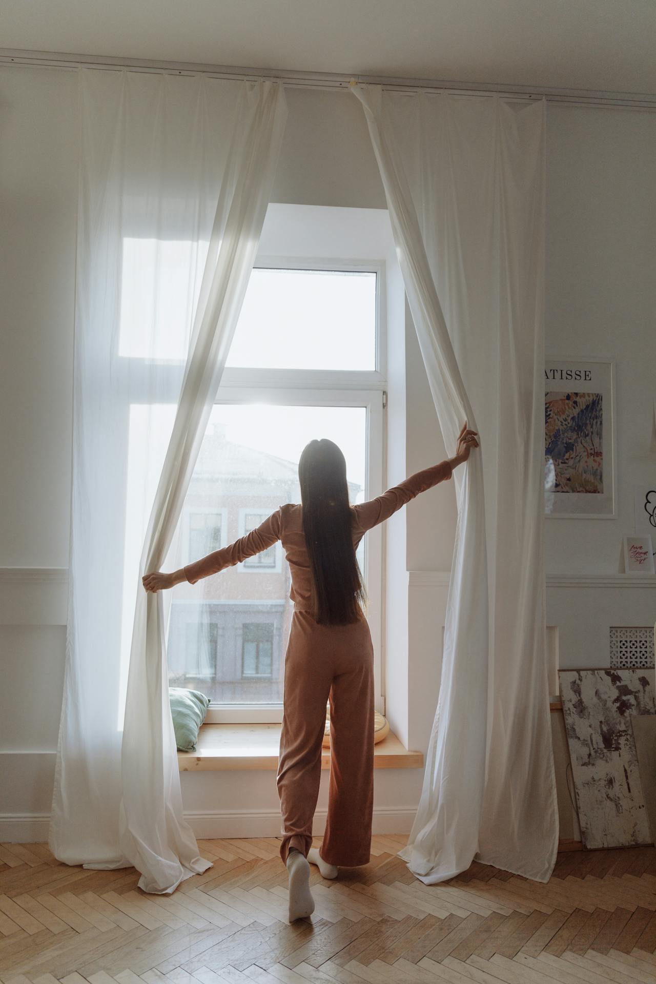 Une femme se tenant près de la fenêtre et ouvrant les rideaux | Source : Pexels