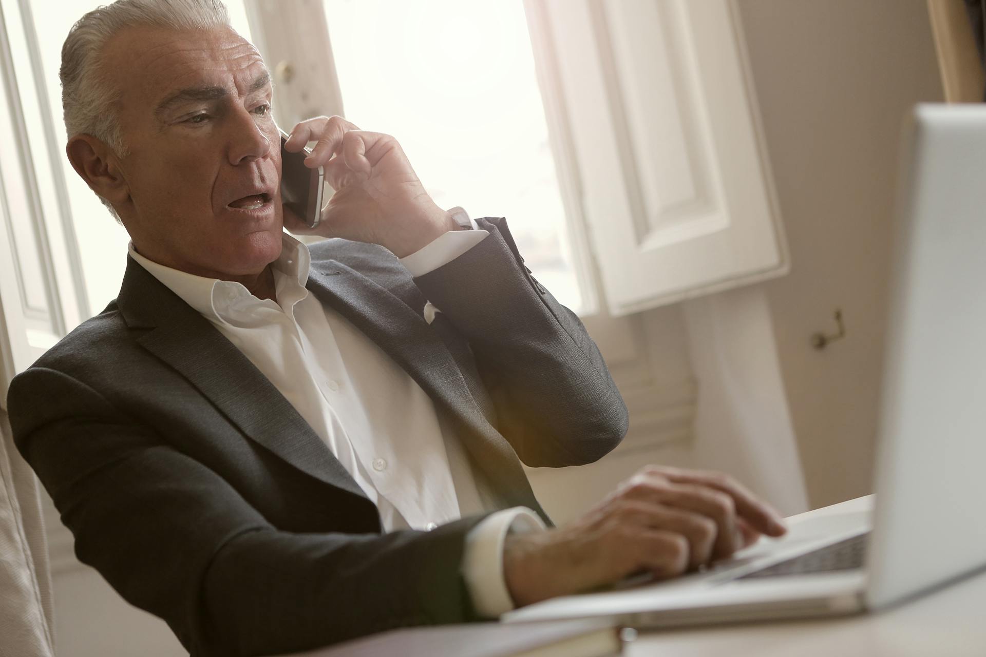 Un homme inquiet parle au téléphone tout en utilisant son ordinateur portable | Source : Pexels
