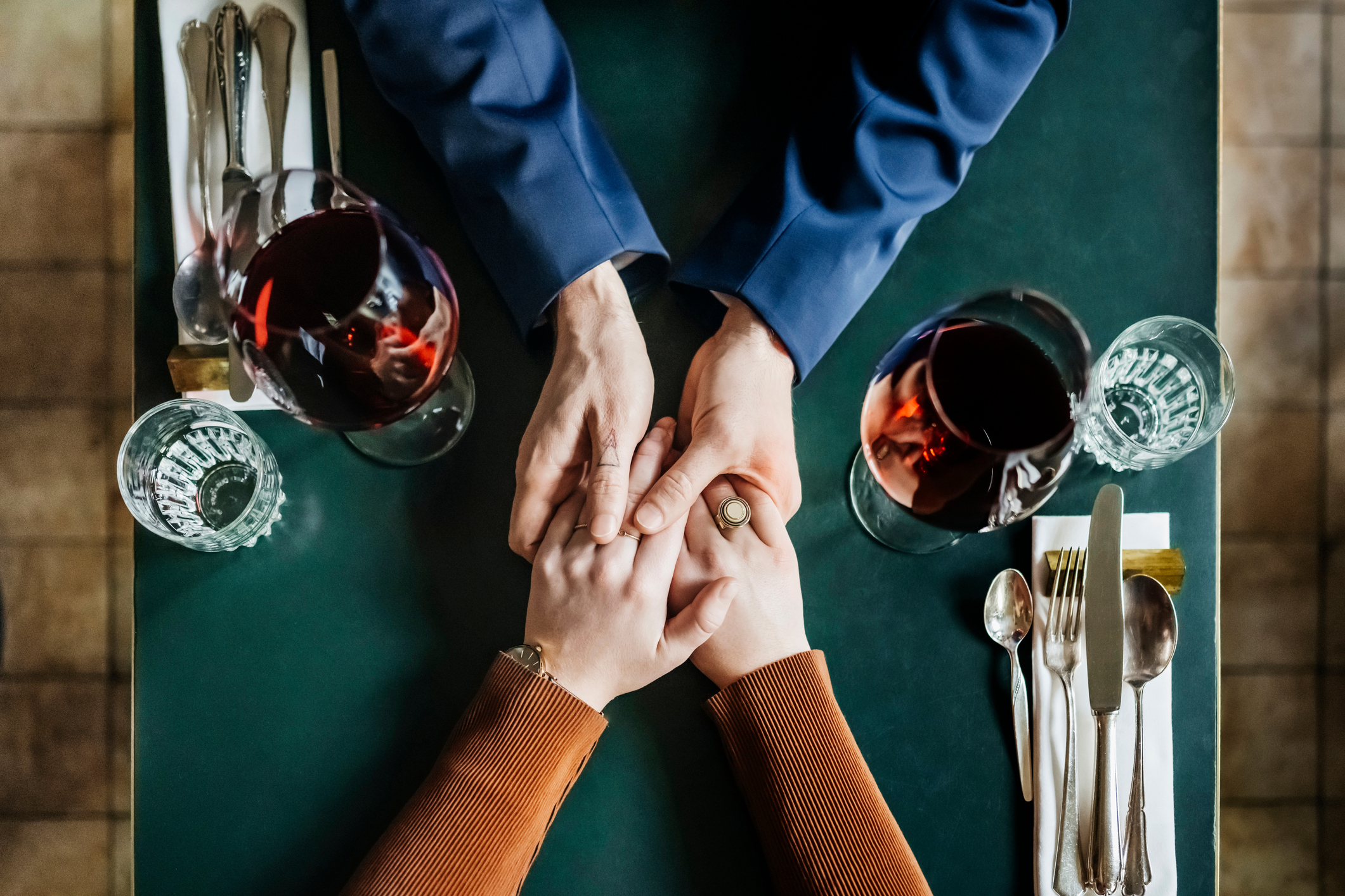 Un couple se tenant la main et buvant du vin rouge alors qu'ils sont assis à la table d'un restaurant I Source : Getty Images