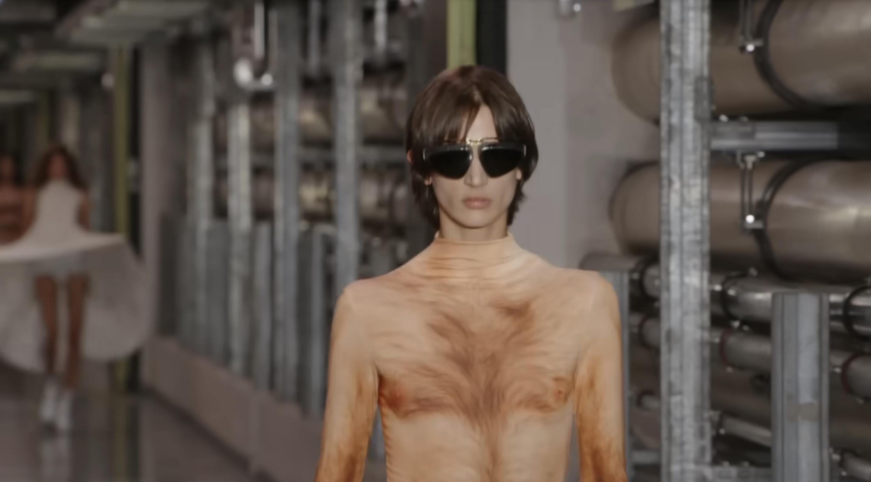 Un gros plan de la caméra révèle toutefois que le mannequin porte en réalité une combinaison sous sa jupe. Celle-ci est assortie à sa couleur de peau et arbore un motif imprimé représentant des poils, créant ainsi l'illusion d'une peau nue. Extrait d'une publication datée du 5 octobre 2025. Source : Youtube/@jeanpaulgaultier