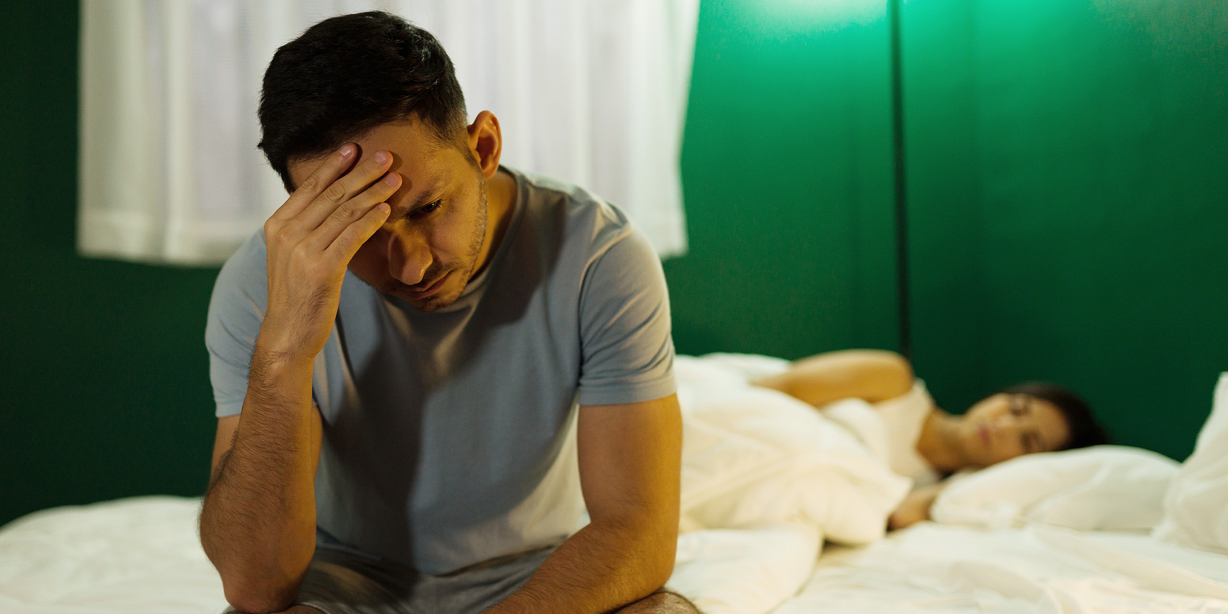Un mari stressé assis sur un lit pendant que sa femme dort | Source : Shutterstock