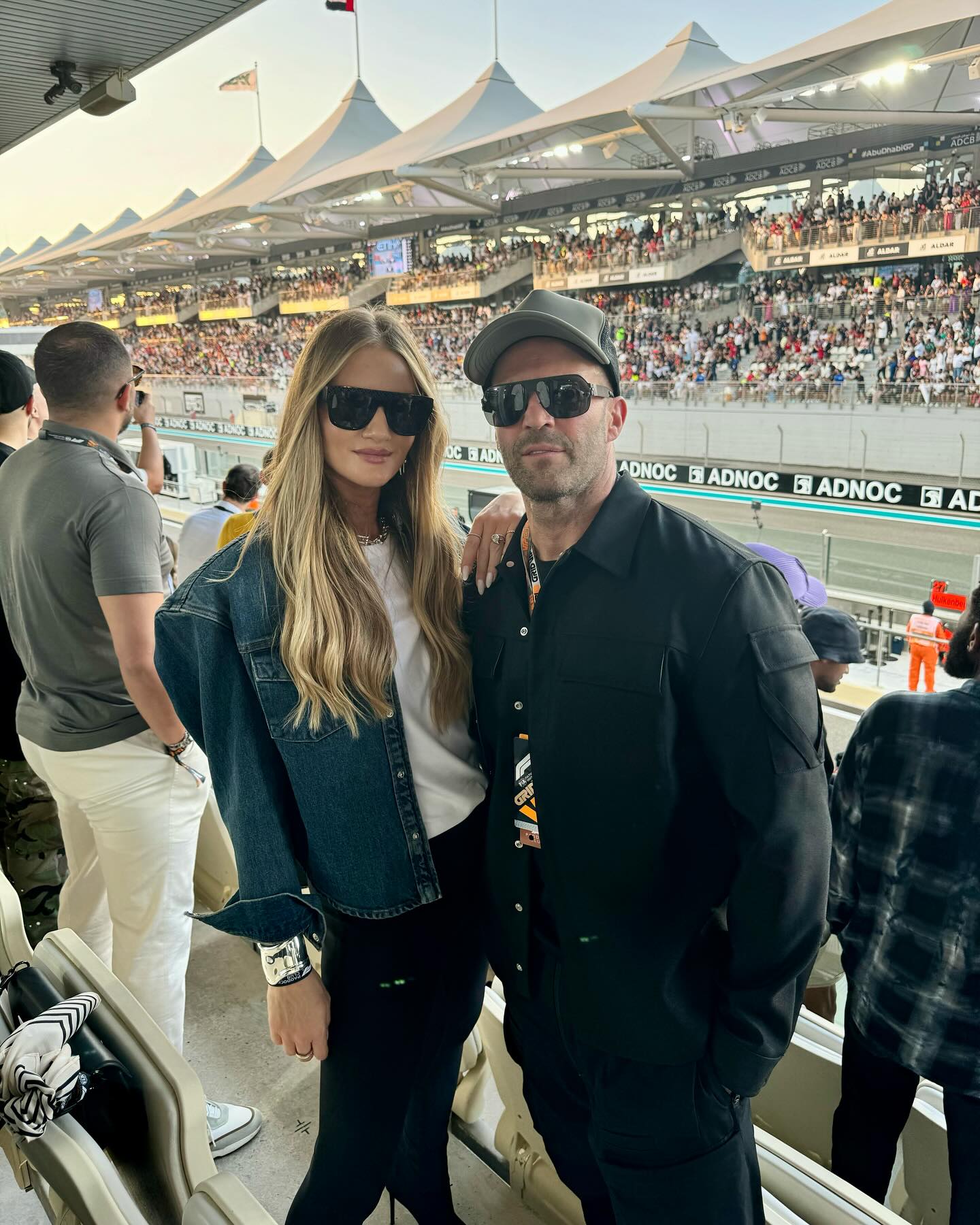Rosie Huntington-Whiteley et Jason Statham posent sur le bord de la piste lors d'une course automobile, arborant tous deux des lunettes de soleil foncées et un look cool sans effort. | Source : Instagram/rosiehw