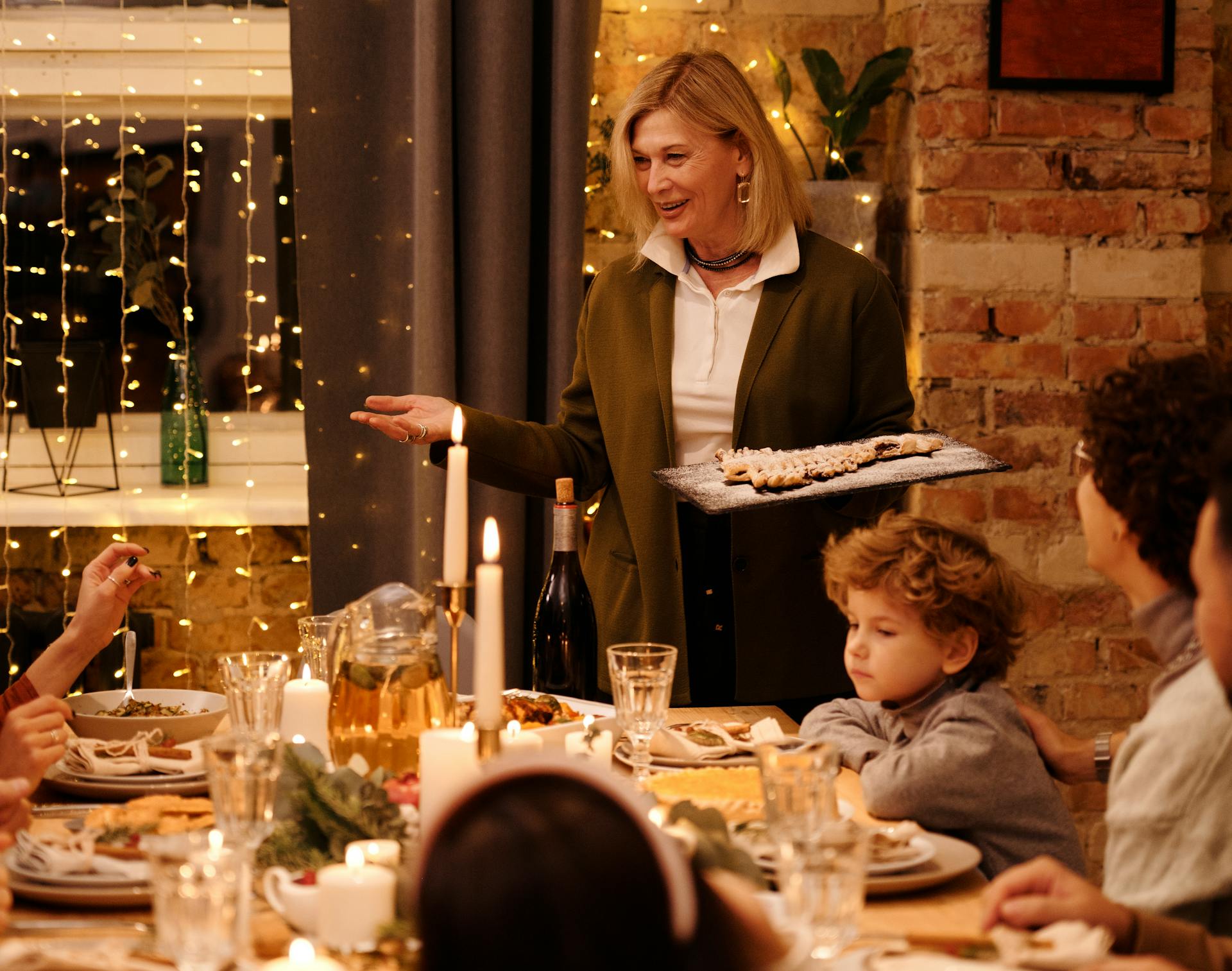 Une femme servant de la nourriture à sa famille à une table à manger avec des bougies et des guirlandes électriques | Source : Pexels