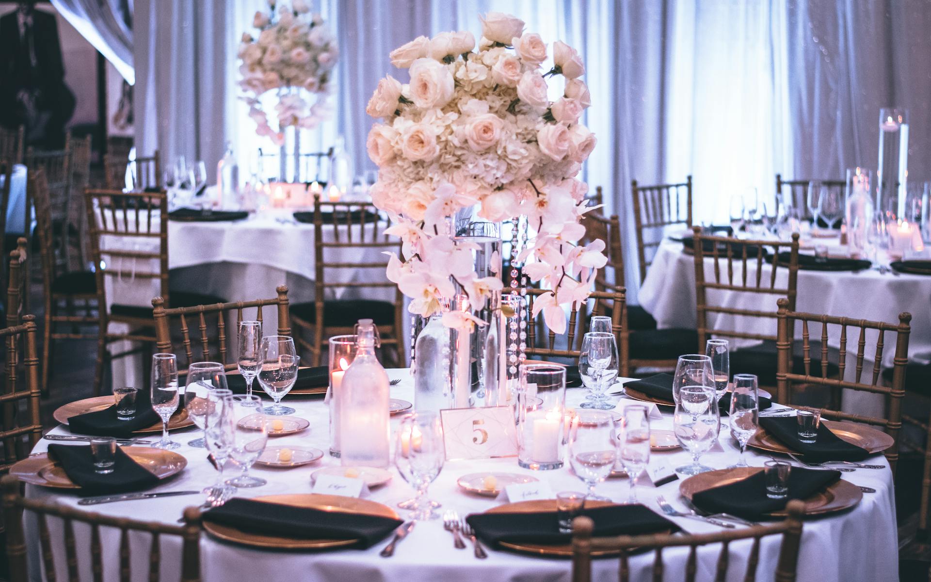 Une table de mariage luxueuse, composée de chaises dorées, d'assiettes noires, et d'un centre de table floral | Source : Pexels
