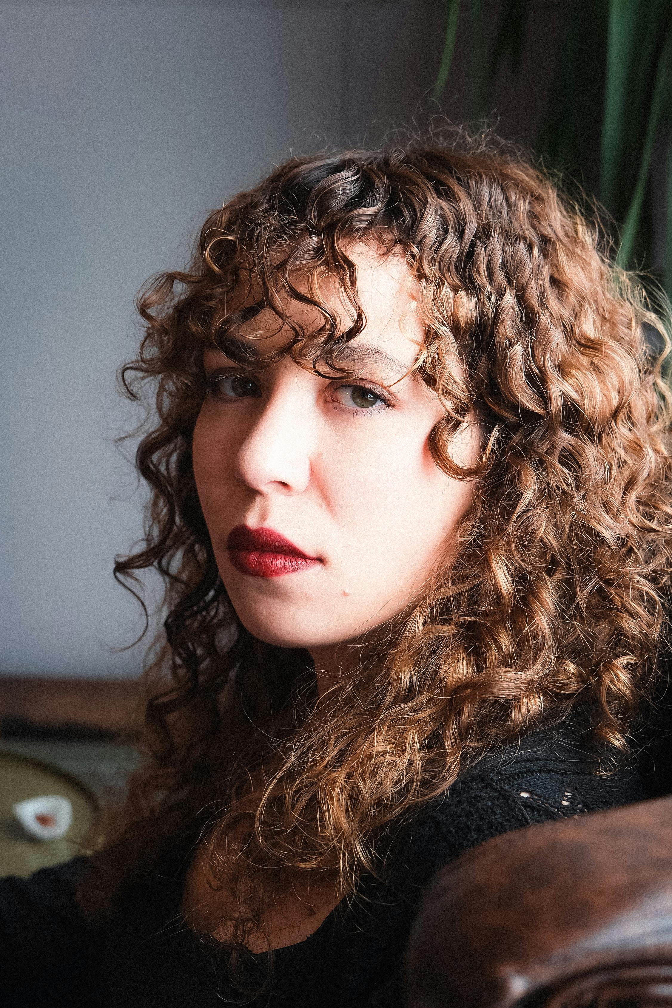 Une femme pensive aux cheveux bouclés et au rouge à lèvres rouge | Source : Pexels