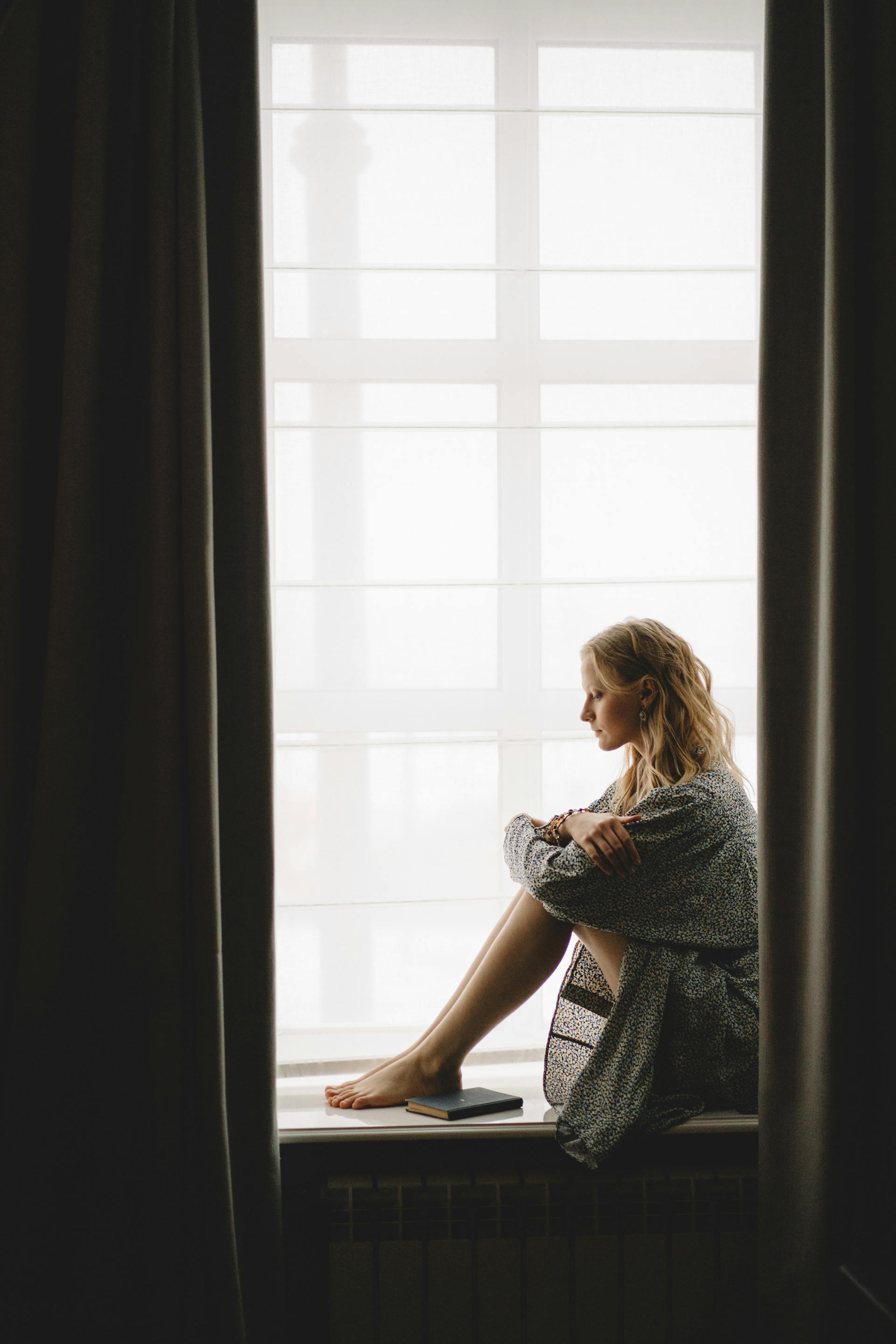 Une femme pensive assise sur le rebord de la fenêtre | Source : Pexels
