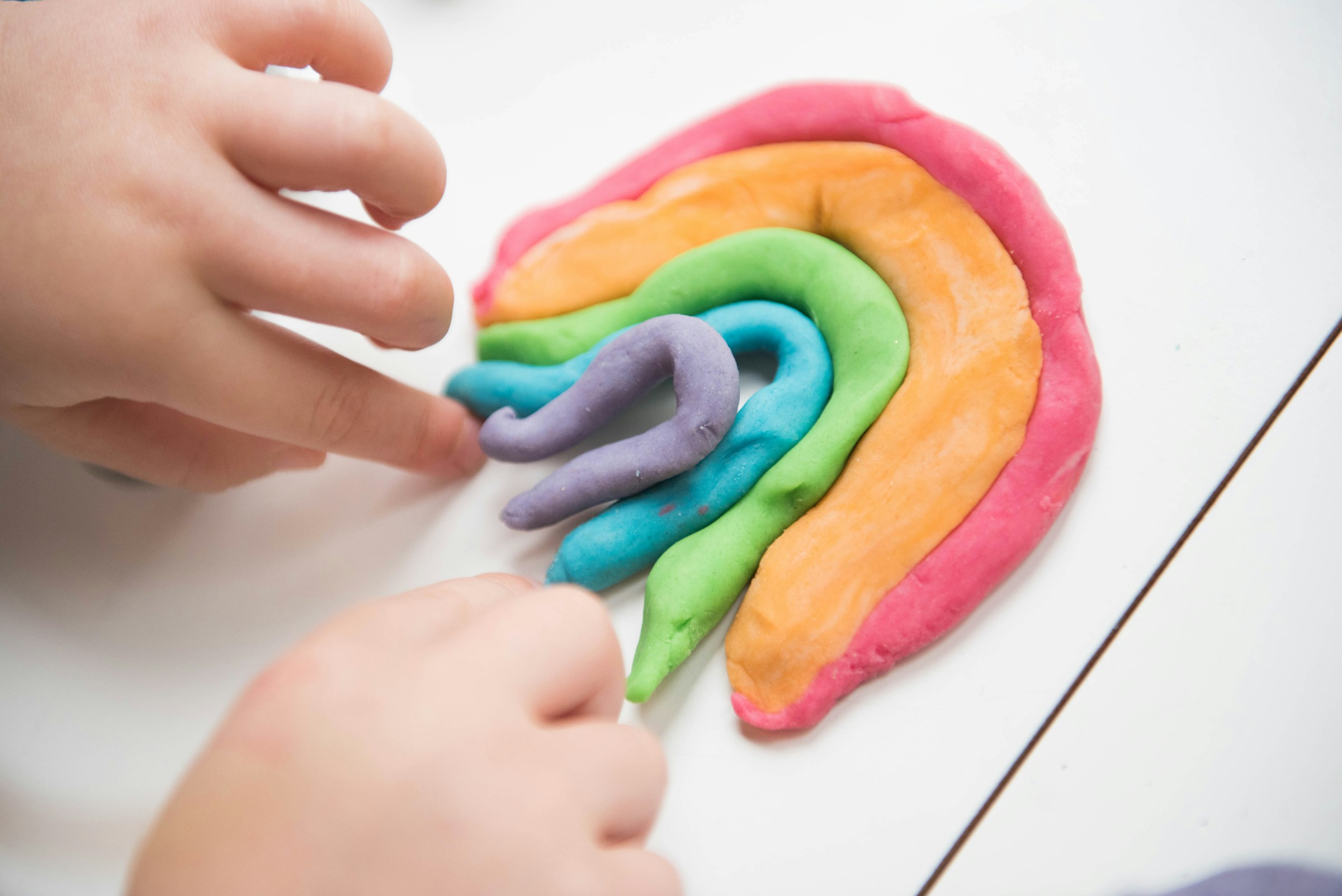 Gros plan d'un enfant jouant avec des bandes colorées de Play-Doh | Source : Unsplash