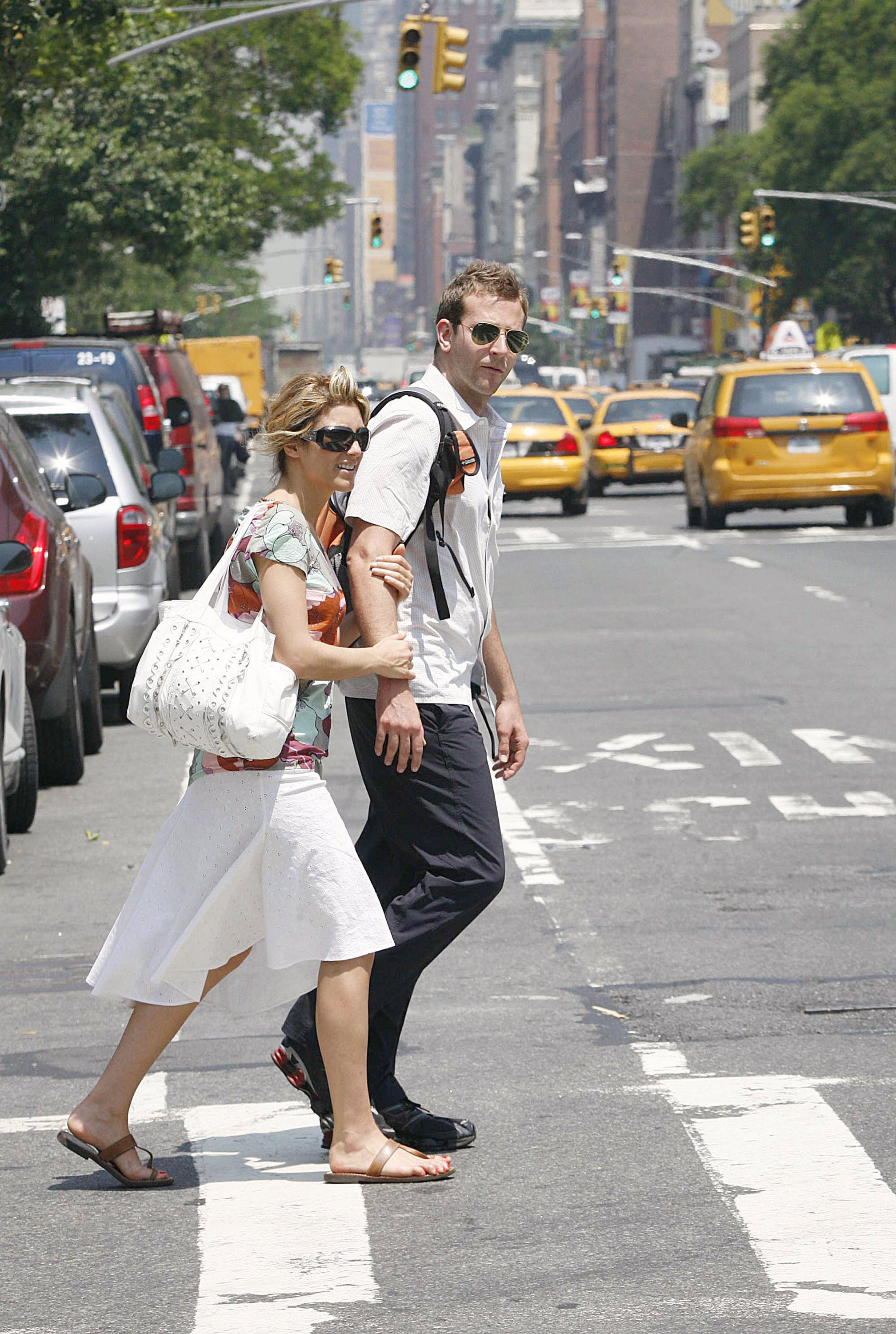 Jennifer Esposito et Bradley Cooper photographiés alors qu'ils traversaient une rue de Manhattan le 30 mai 2006. Esposito portait une jupe blanche et un chemisier à fleurs, des lunettes de soleil oversize et un sac à main blanc, tandis que Cooper marchait à ses côtés vêtu d'un pantalon foncé et d'une chemise à manches courtes boutonnée, avec un sac à dos, quelques mois avant leurs fiançailles.