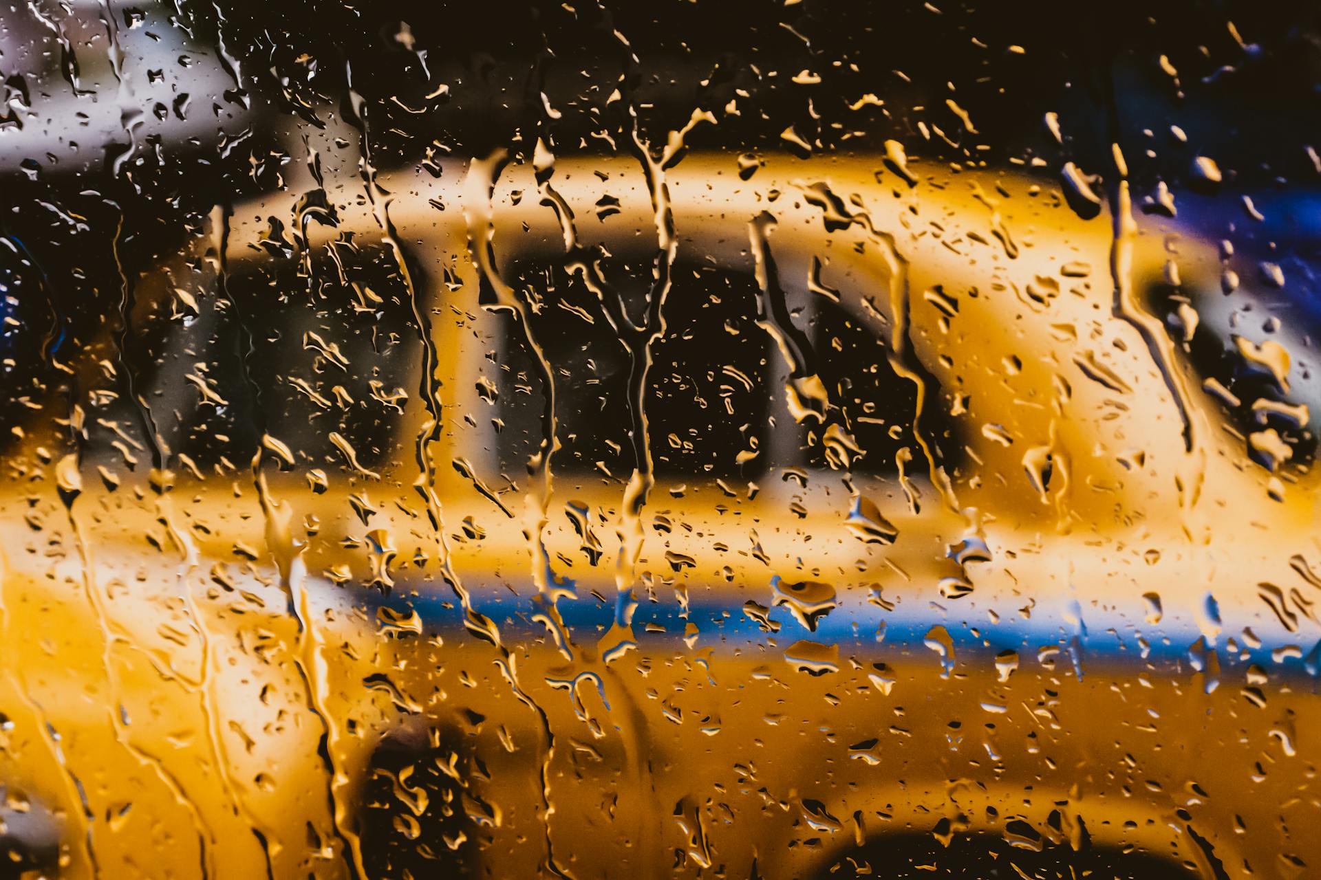 Une fenêtre mouillée avec une voiture jaune floue derrière elle | Source : Pexels