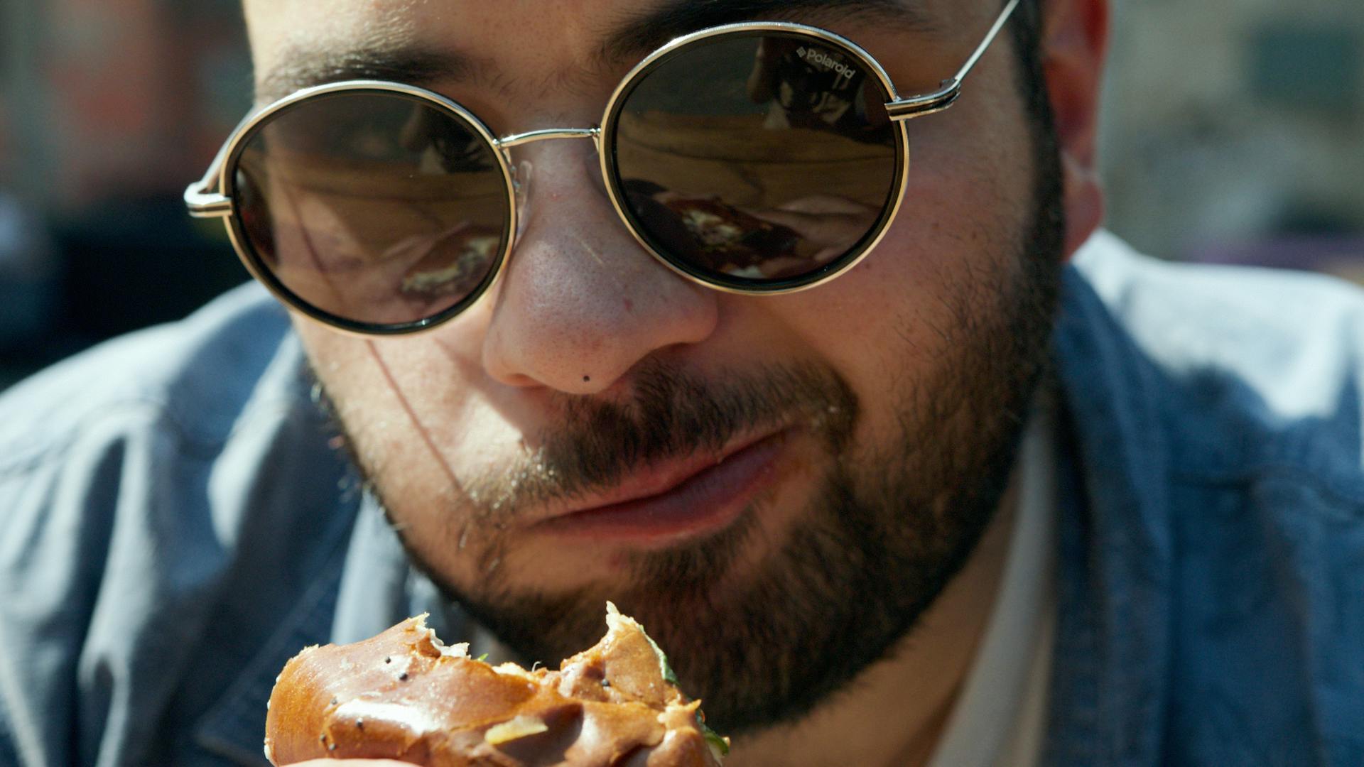Un homme portant des lunettes à monture noire mangeant une pizza | Source : Pexels