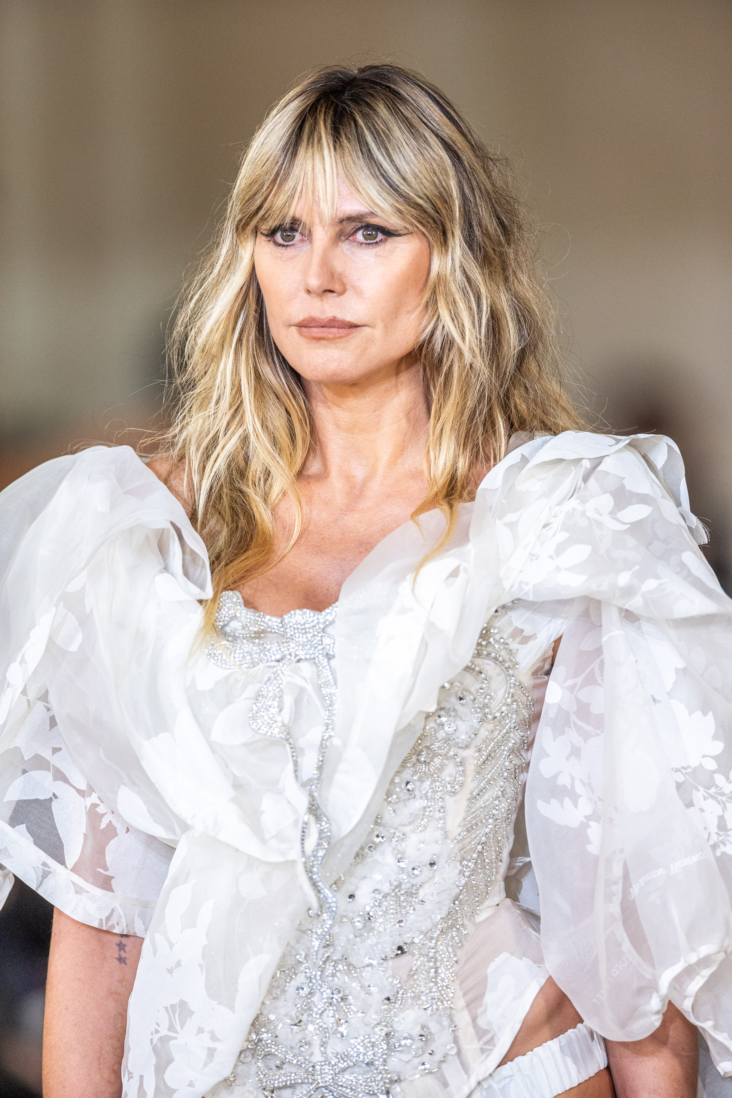 Heidi Klum a défilé lors du défilé prêt-à-porter printemps/été 2026 de Vivienne Westwood pendant la Fashion Week de Paris, en France, vêtue d'une robe blanche. Le corsage était orné de filigranes argentés et comportait un nœud décoré de bijoux sur le décolleté plongeant. Le tissu brodé blanc transparent ajoutait des manches bouffantes et un détail semblable à une cape, rehaussant l'élégance spectaculaire de son look.