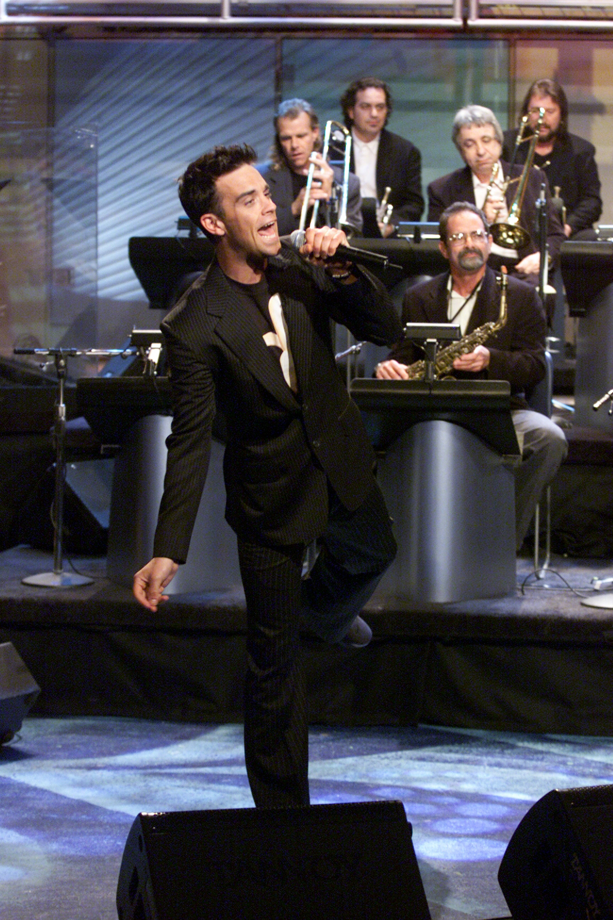 Robbie Williams se produit dans « The Tonight Show with Jay Leno » le 26 avril 2001, arborant son style caractéristique dans un costume rayé. Accompagné par le groupe maison, ce concert marque un moment décisif dans sa conquête du marché américain.