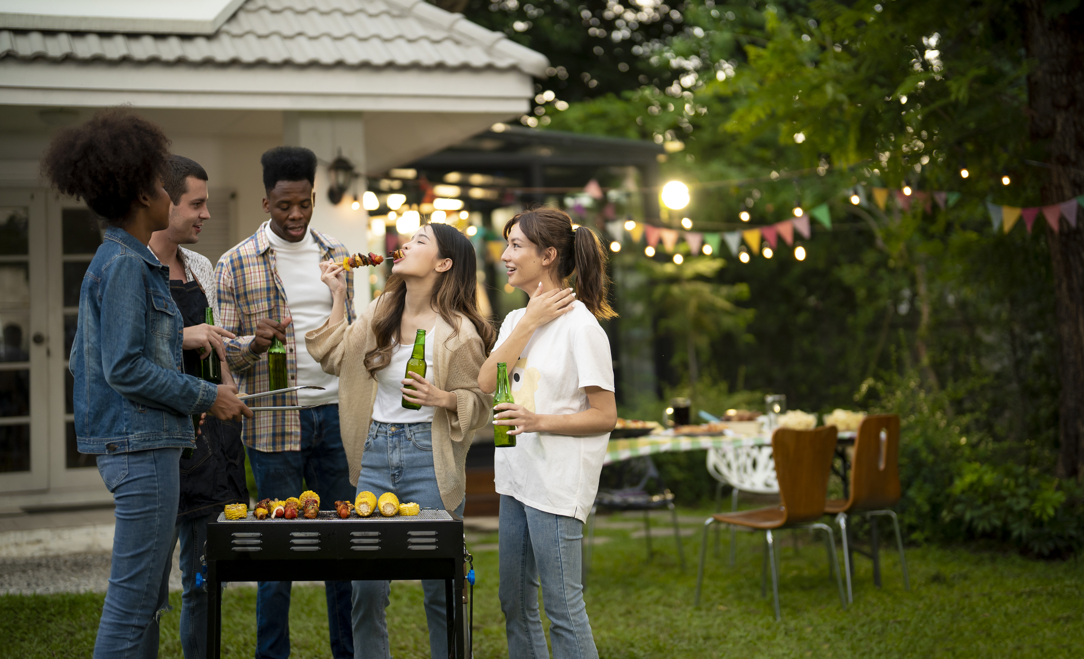 Groupe de jeunes mangeant lors d'un barbecue dans un jardin I Source : Getty Images