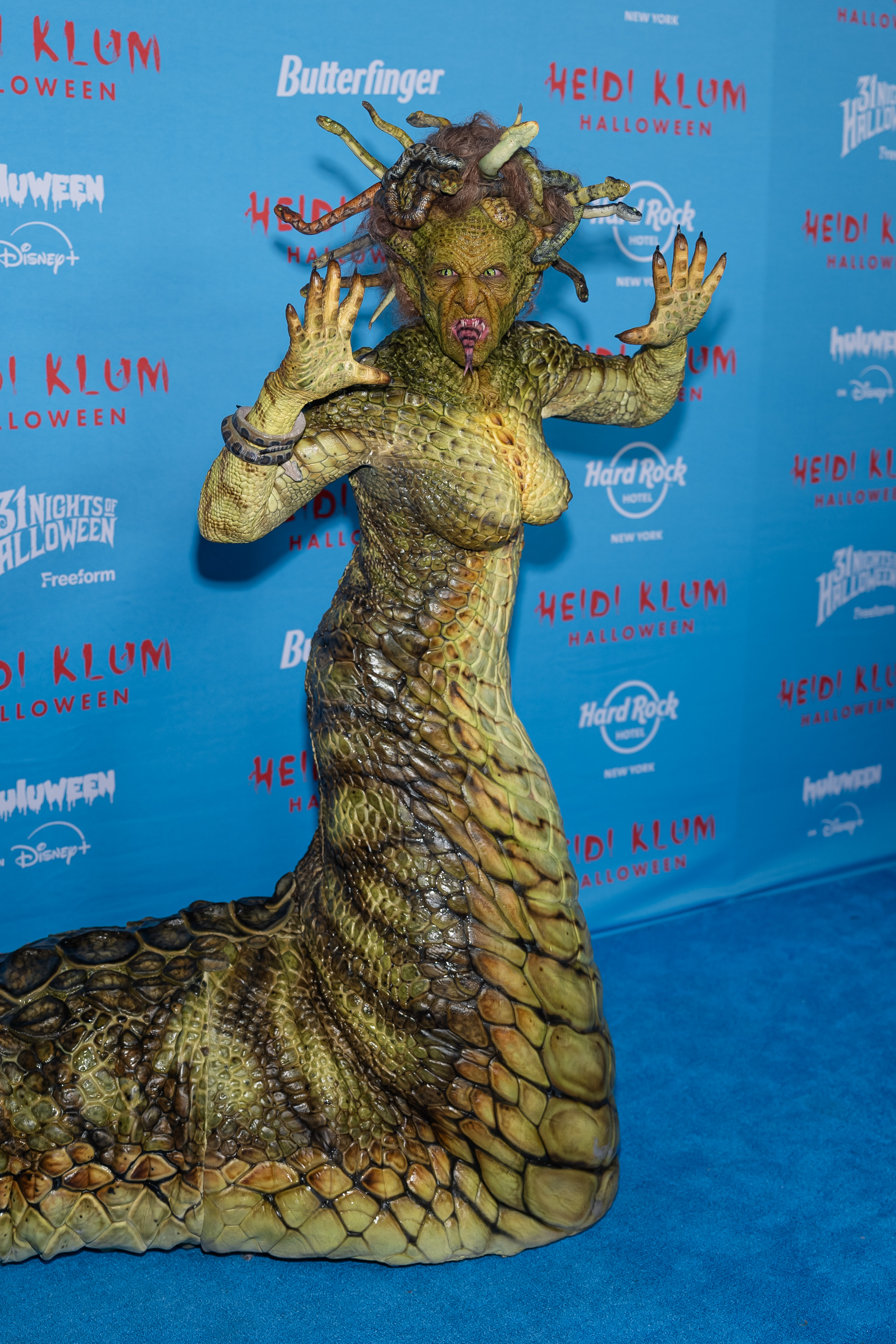 Lors de sa 24e fête annuelle d'Halloween à New York, Klum a fait sensation dans un costume intégral de Méduse qui brouillait les frontières entre la mode et le design créature. Recouverte d'écailles reptiliennes hyper détaillées, elle s'est glissée sur le tapis bleu avec une queue de serpent réaliste et une coiffe composée de serpents grondants. Des lentilles de contact jaunes reptiliennes et des prothèses à crocs complétaient ce look terrifiant inspiré des mythes, une nouvelle transformation extravagante de la reine incontestée d'Halloween.