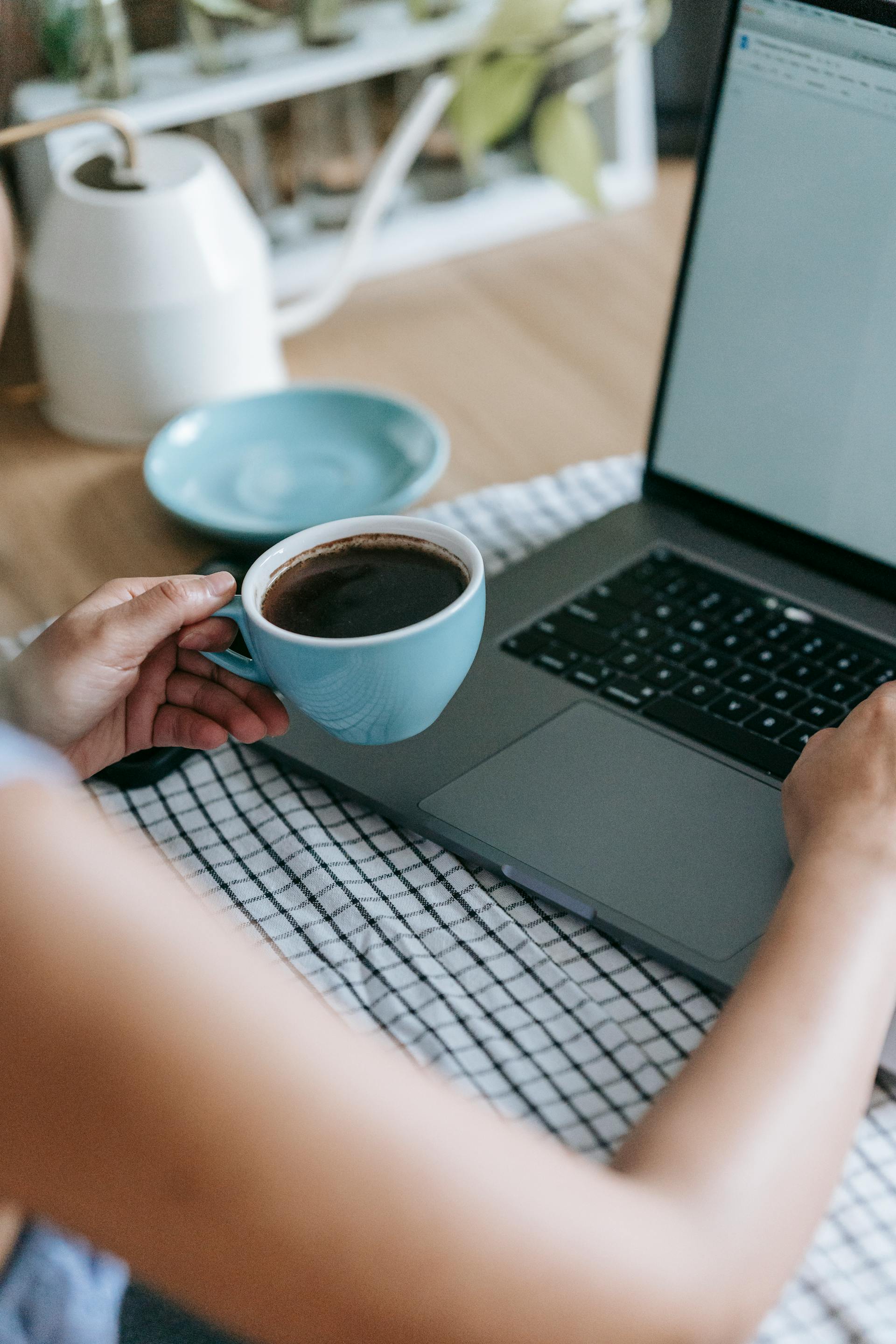 Une femme tenant une tasse de café tout en utilisant son ordinateur portable | Source : Pexels