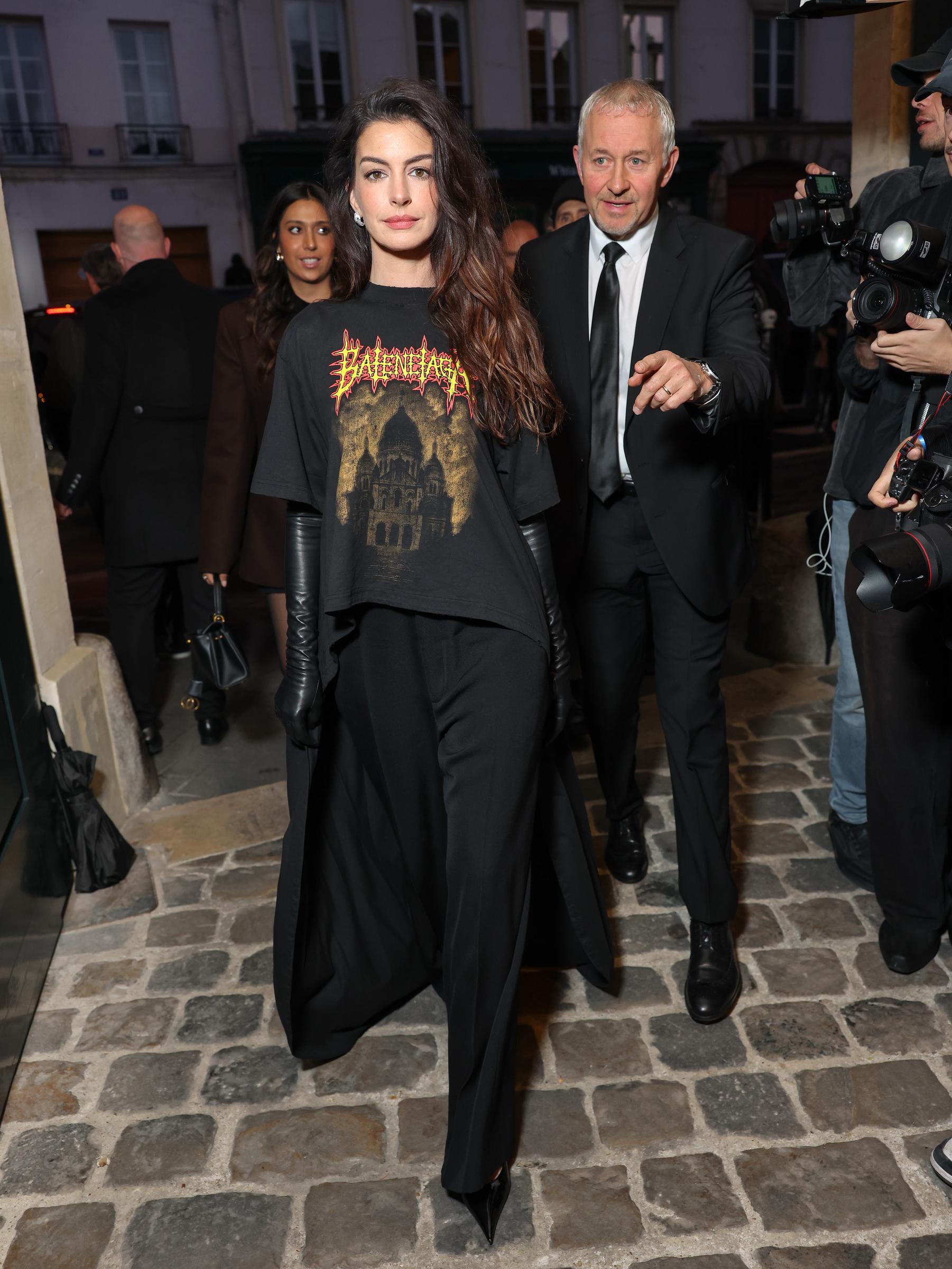 Anne Hathaway assiste au défilé Balenciaga Femme Printemps/Été 2026 lors de la Fashion Week de Paris en France. Elle porte un t-shirt graphique orné d'un logo métallique et d'un motif mullet, avec une traîne fluide spectaculaire. Elle a complété sa tenue avec un pantalon noir, des gants en cuir et des chaussures pointues.