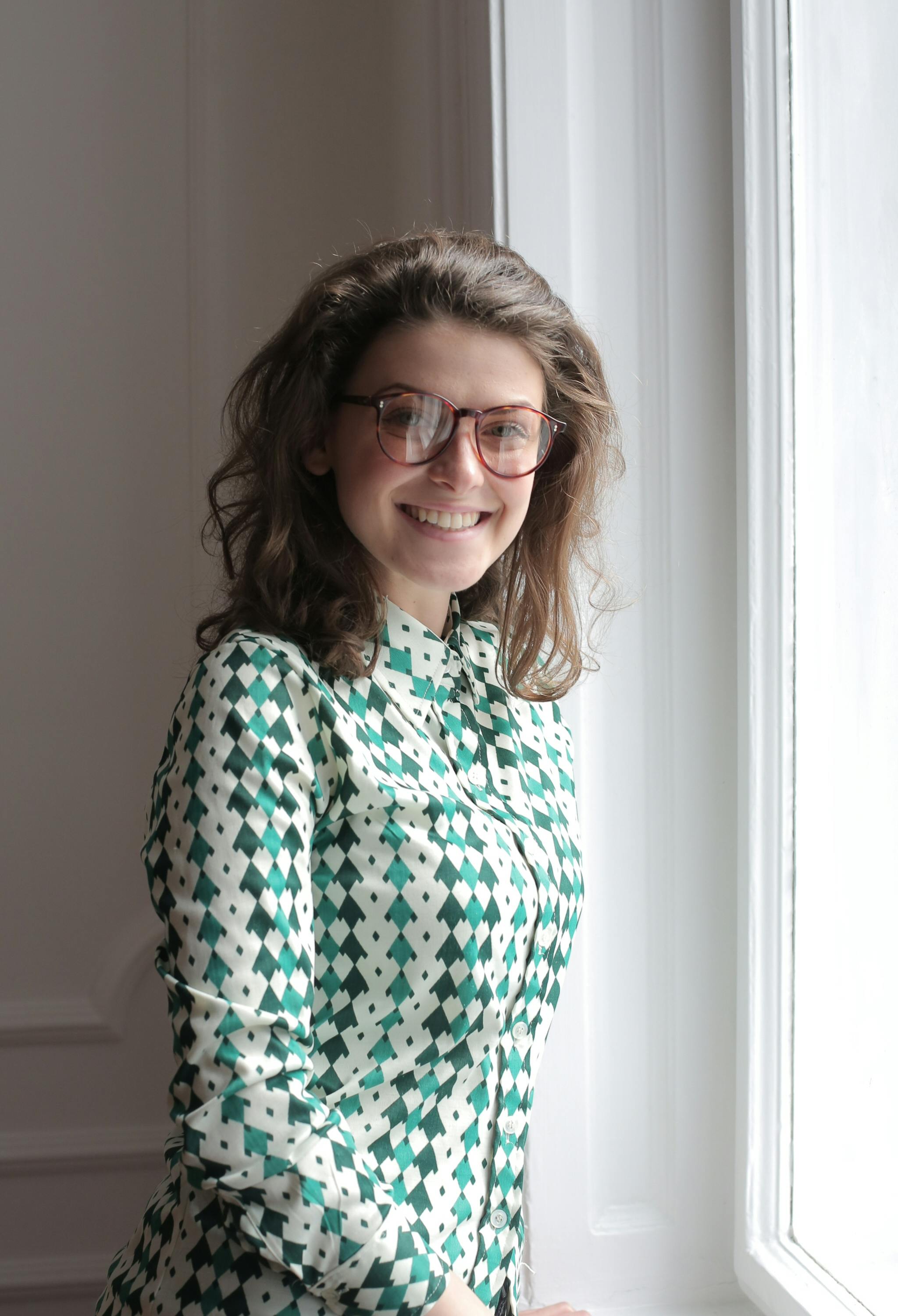 Une femme souriante debout près d'une fenêtre | Source : Pexels