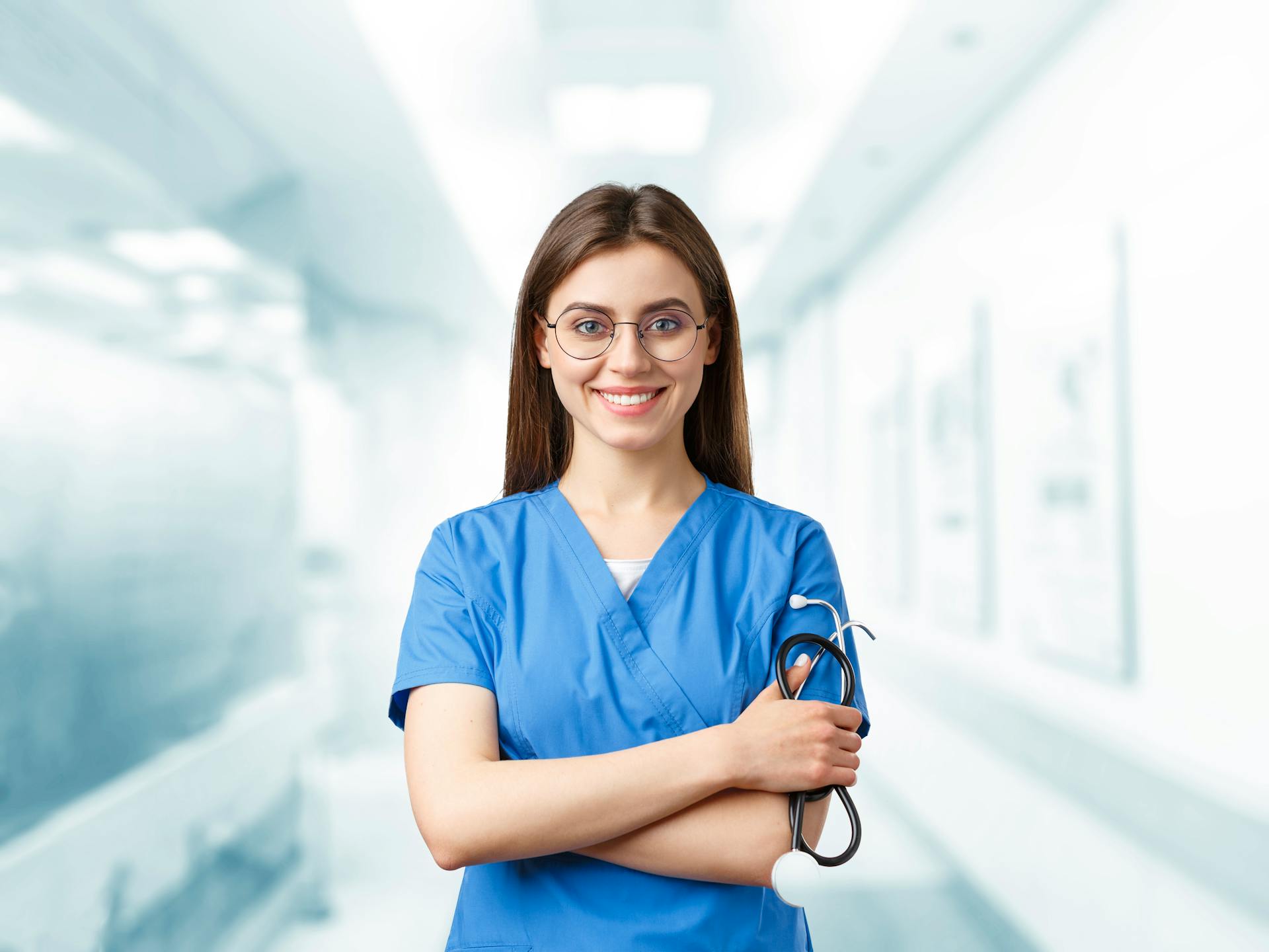 Une jeune femme en blouse bleue sourit en tenant un stéthoscope | Source : Pexels