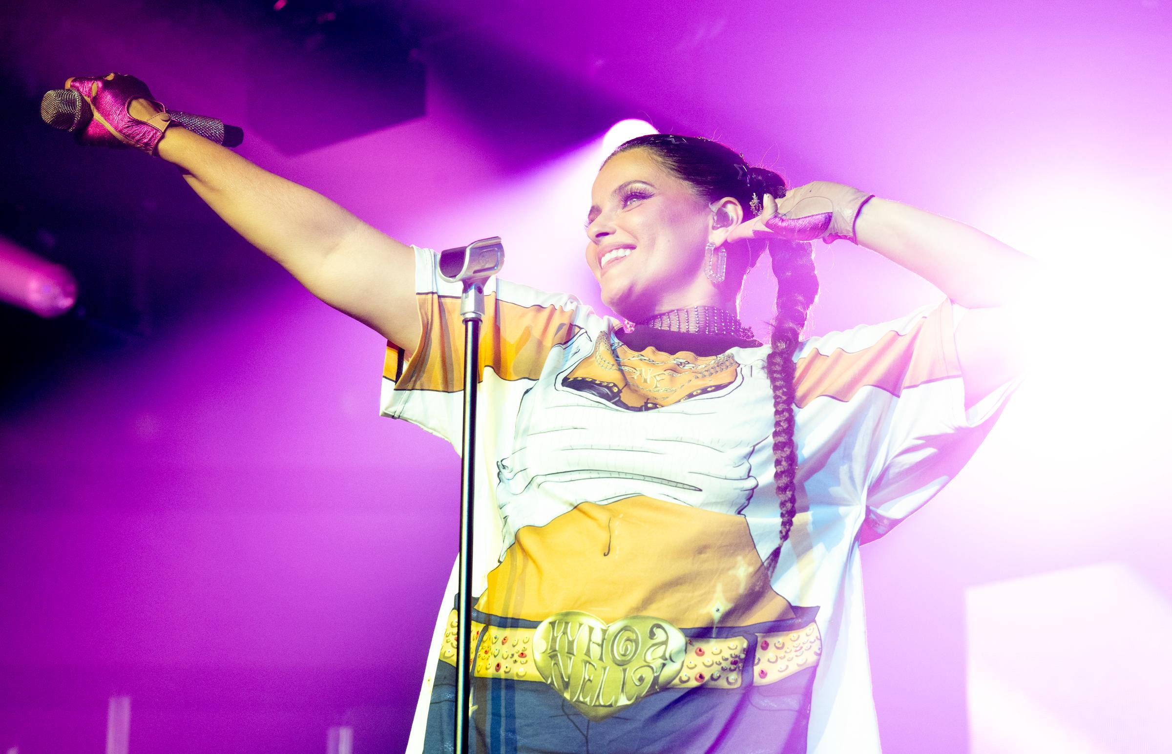Furtado se produit dans un t-shirt oversize imprimé d'un dessin animé, avec un crop top et une mini-jupe en jean, ainsi qu'une ceinture graphique « Whoa Nelly ». Elle porte des gants sans doigts de couleur vive et des tresses, et se tient debout sous un éclairage rose avec un large sourire.
