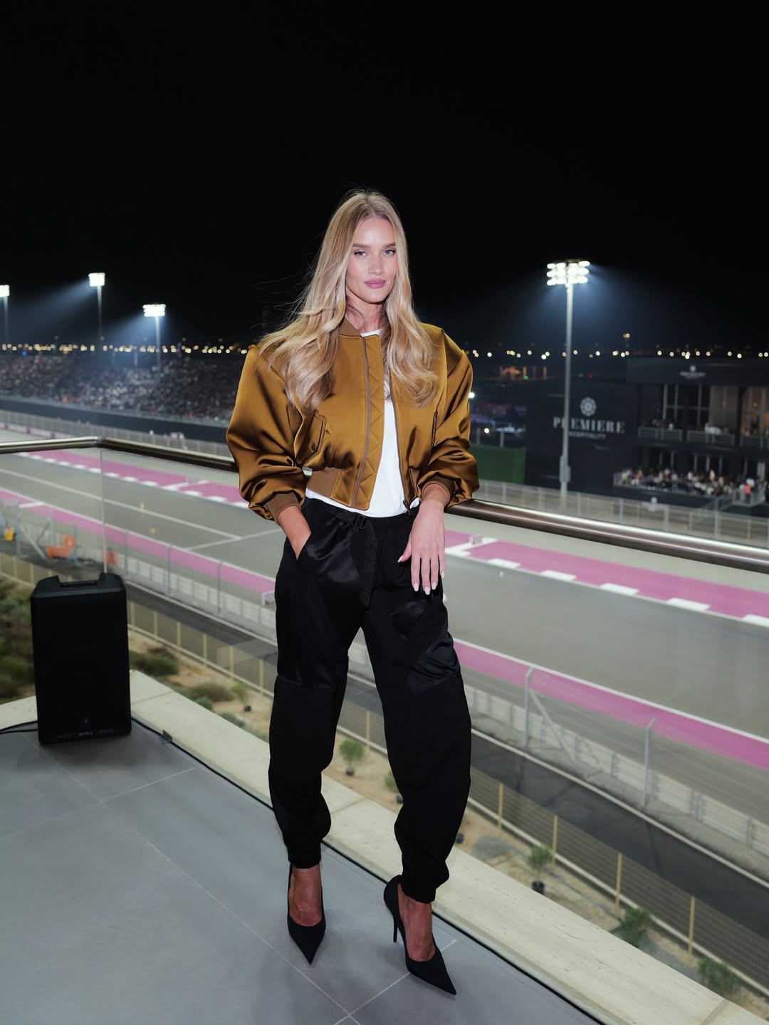 Rosie Huntington-Whiteley pose sur un balcon surplombant un hippodrome éclairé la nuit, mêlant glamour sportif et élégance sans effort. | Source : Instagram/rosiehw