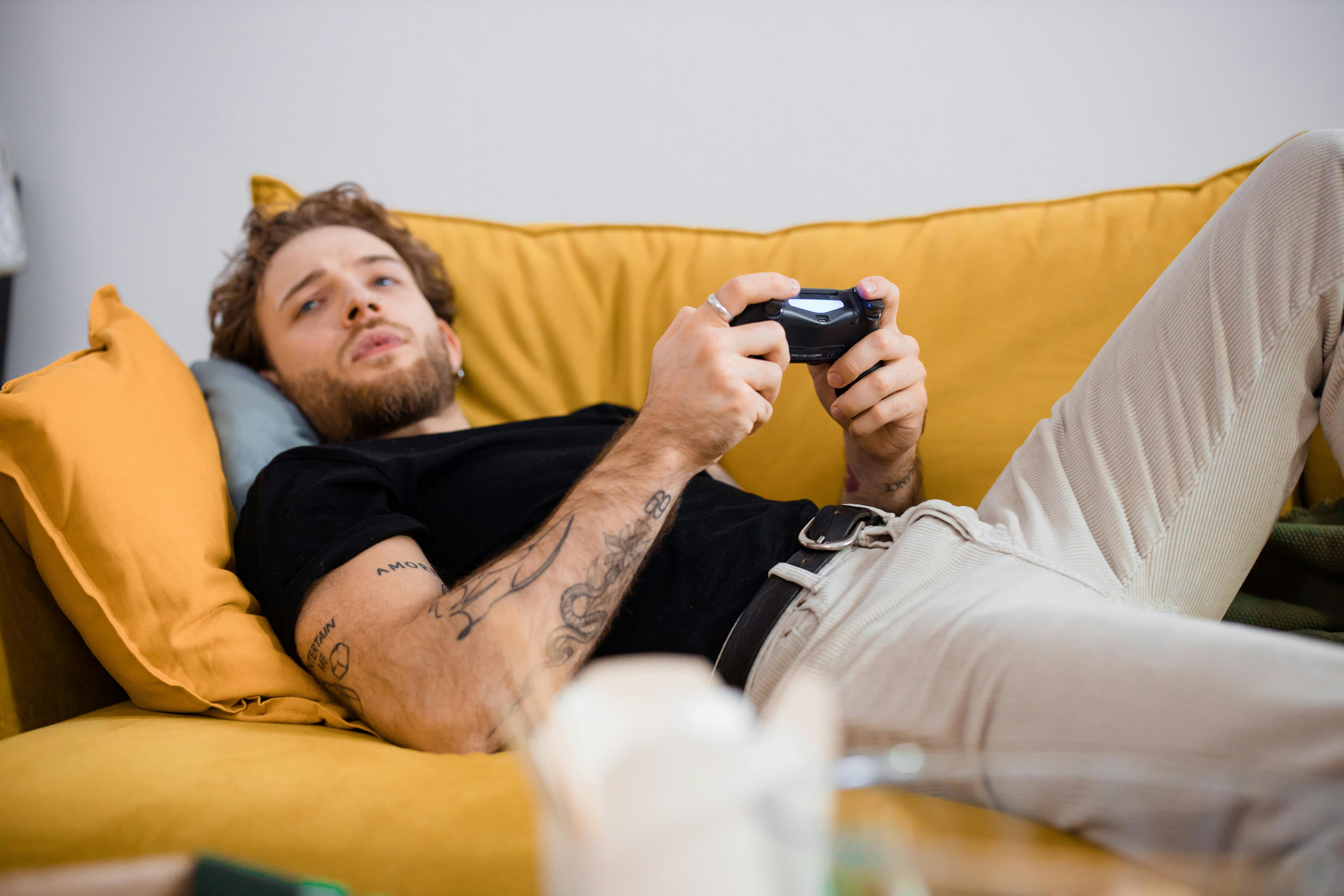 Un homme jouant à un jeu tout en étant allongé sur un canapé | Source : Pexels