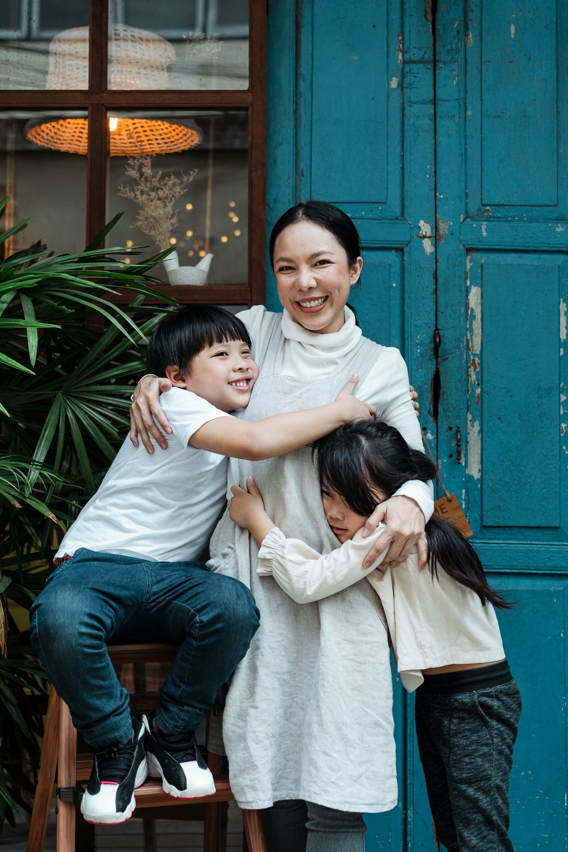 Une mère heureuse embrassant ses deux enfants tout en se tenant devant une porte bleue | Source : Pexels