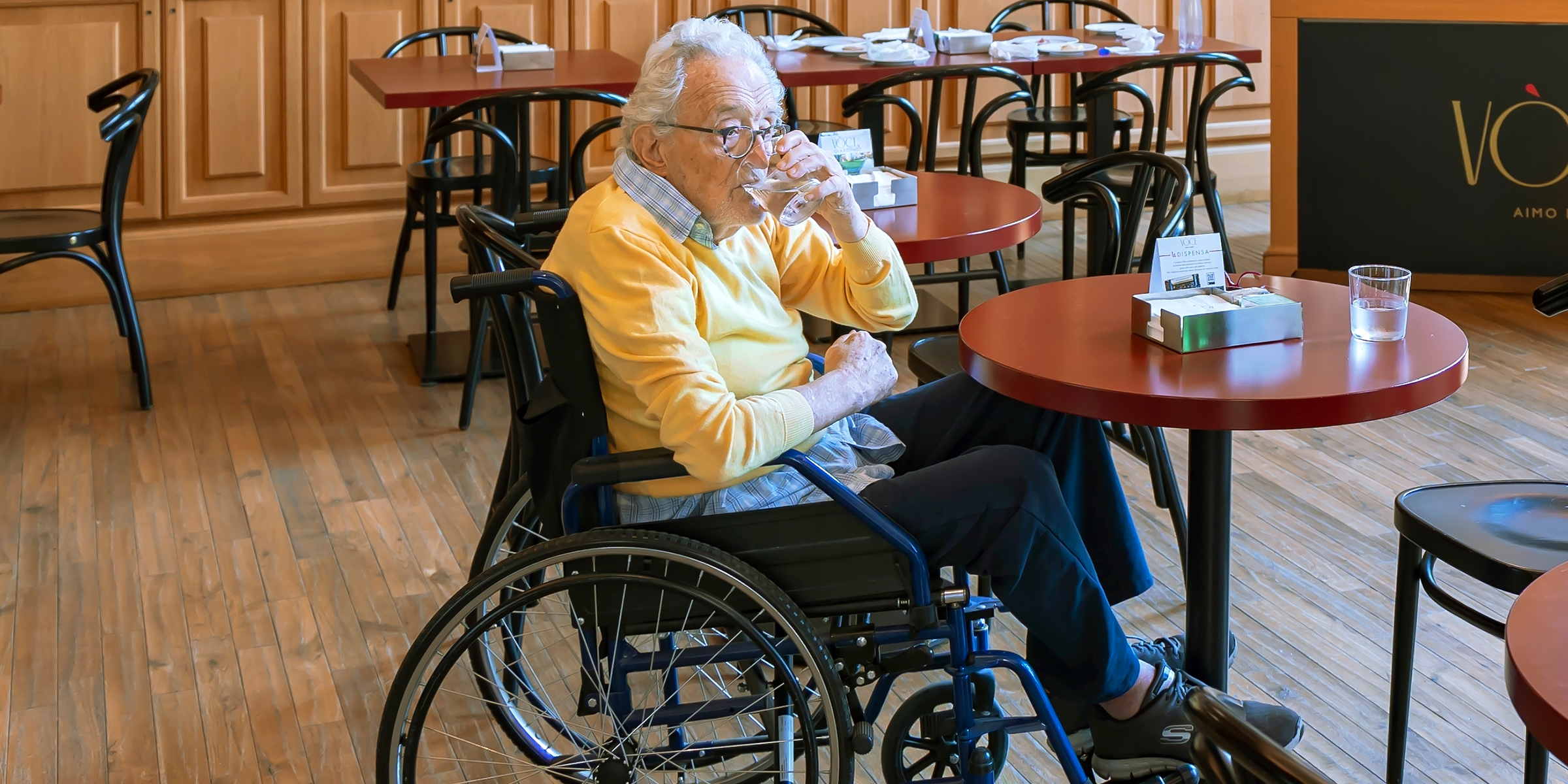 Un homme âgé en fauteuil roulant qui boit de l'eau dans un restaurant | Source : Shutterstock