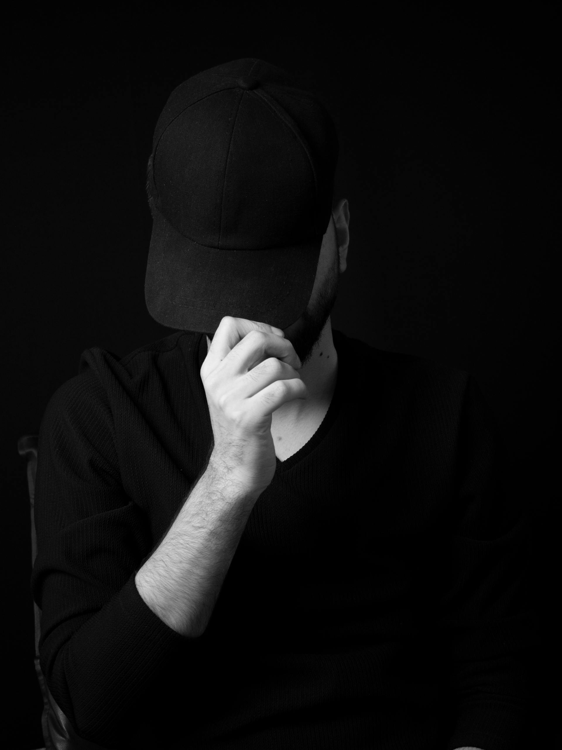 Photo en niveaux de gris d'un homme cachant son visage avec sa casquette | Source : Pexels