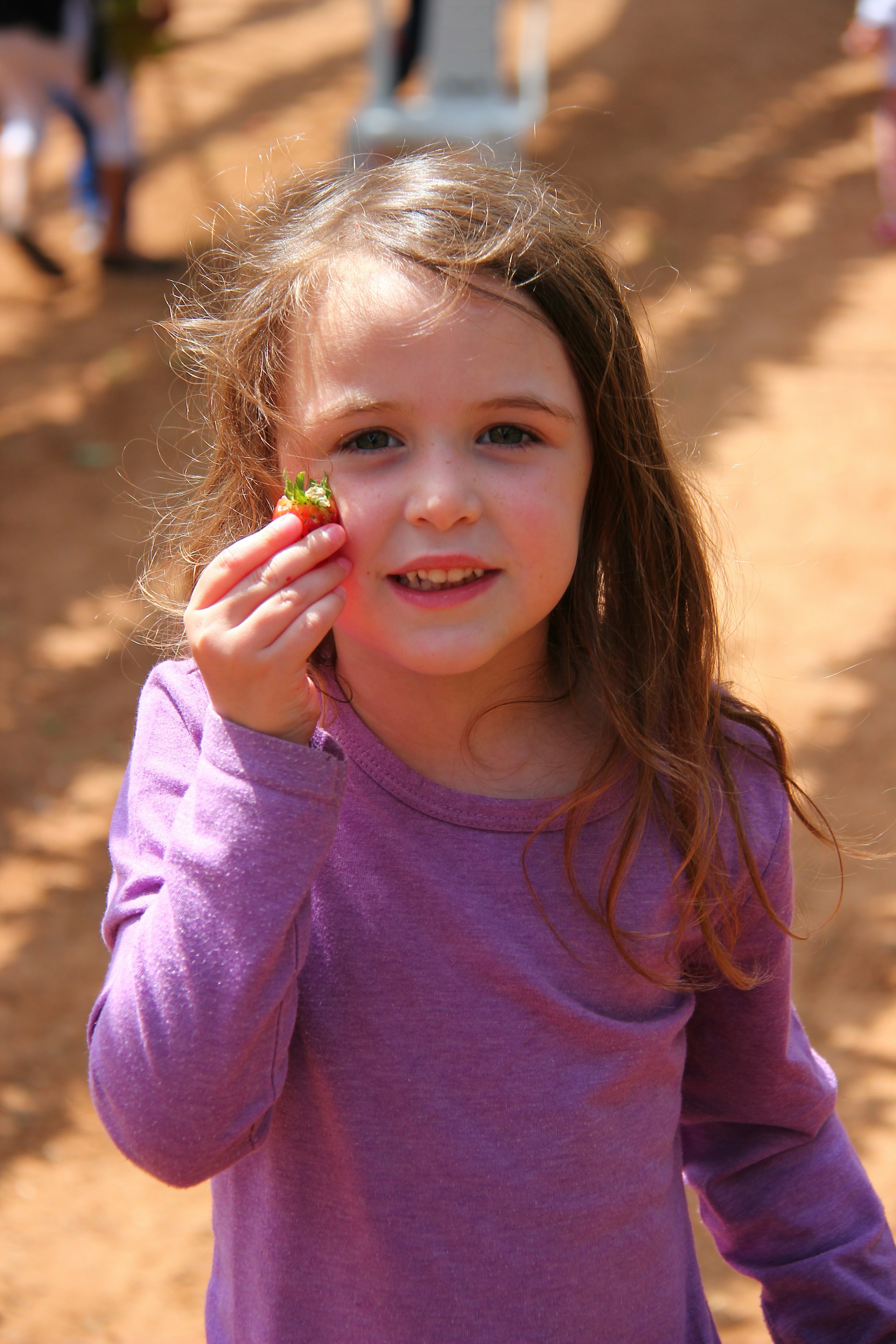 Une petite fille tenant une fraise et souriant | Source : Unsplash