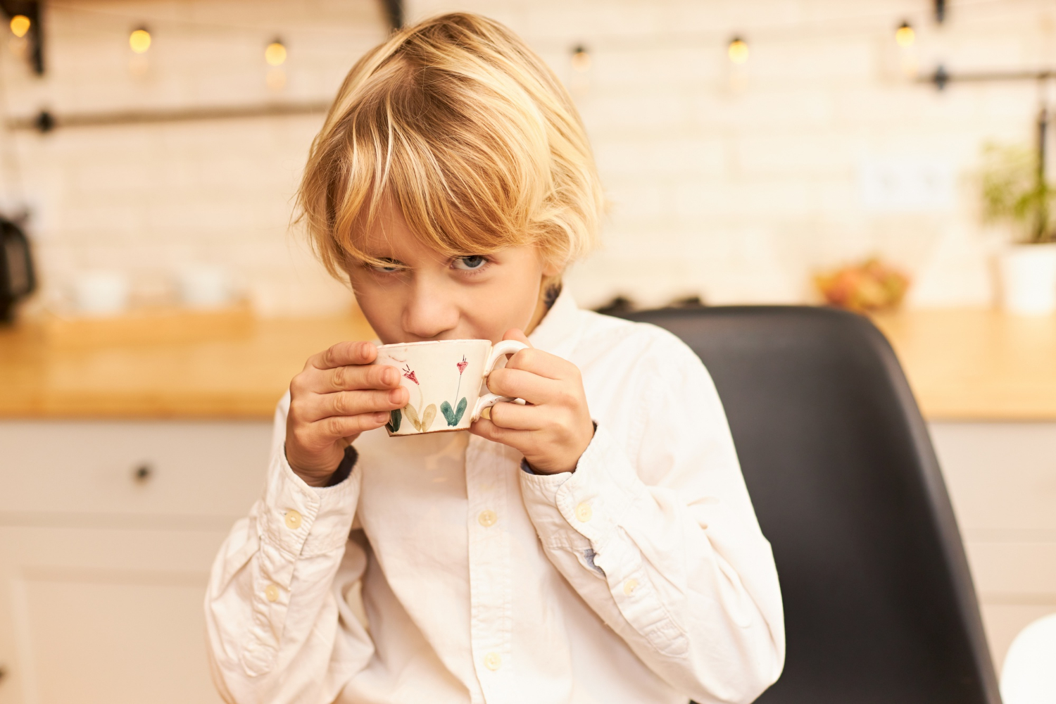 Un petit garçon qui boit dans une tasse en céramique tout en regardant curieusement | Source : Freepik