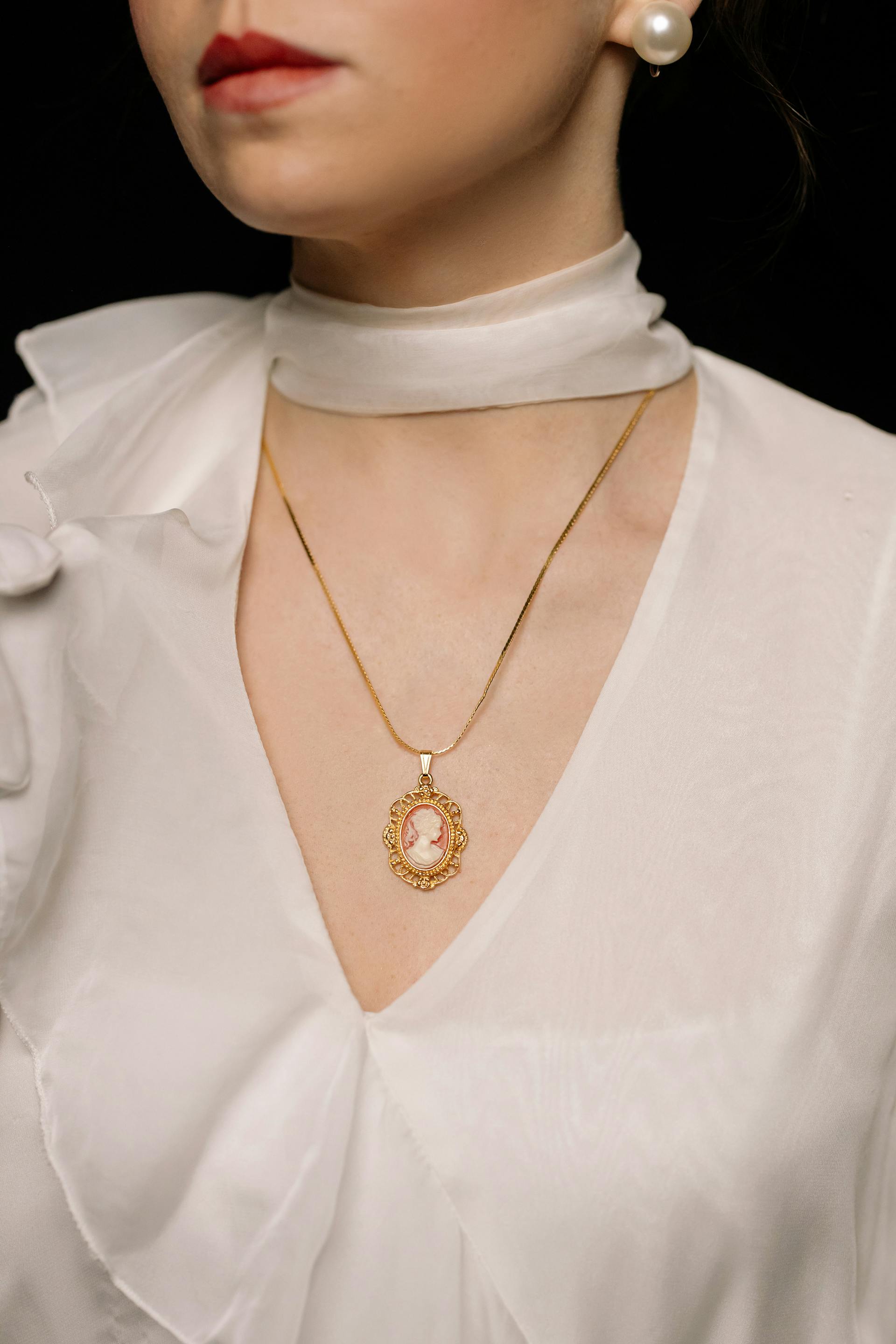 Gros plan d'une femme portant des boucles d'oreilles en perles et un collier en or avec un pendentif | Source : Pexels