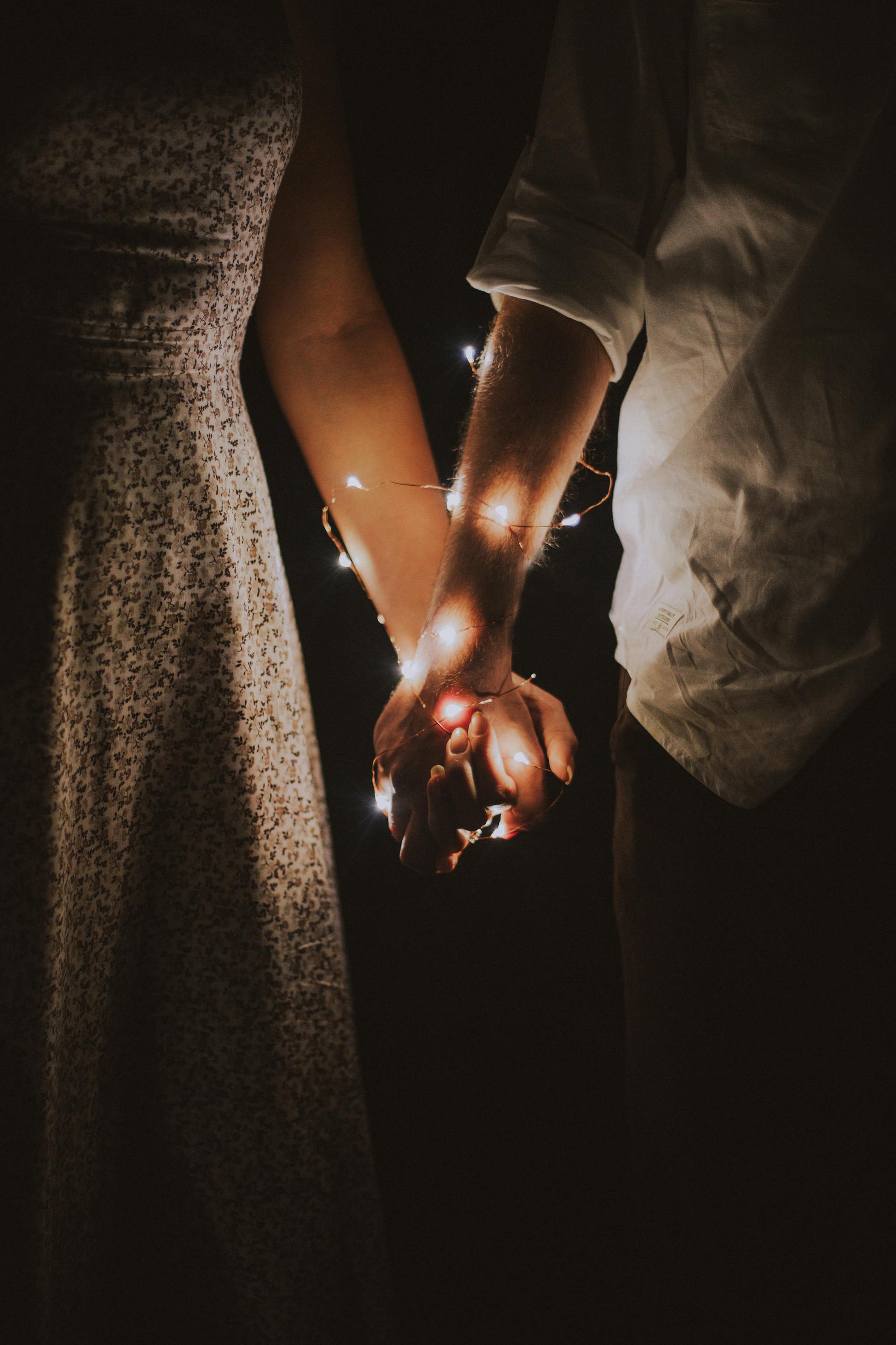 Un couple se tenant par la main enveloppé de guirlandes lumineuses | Source : Pexels