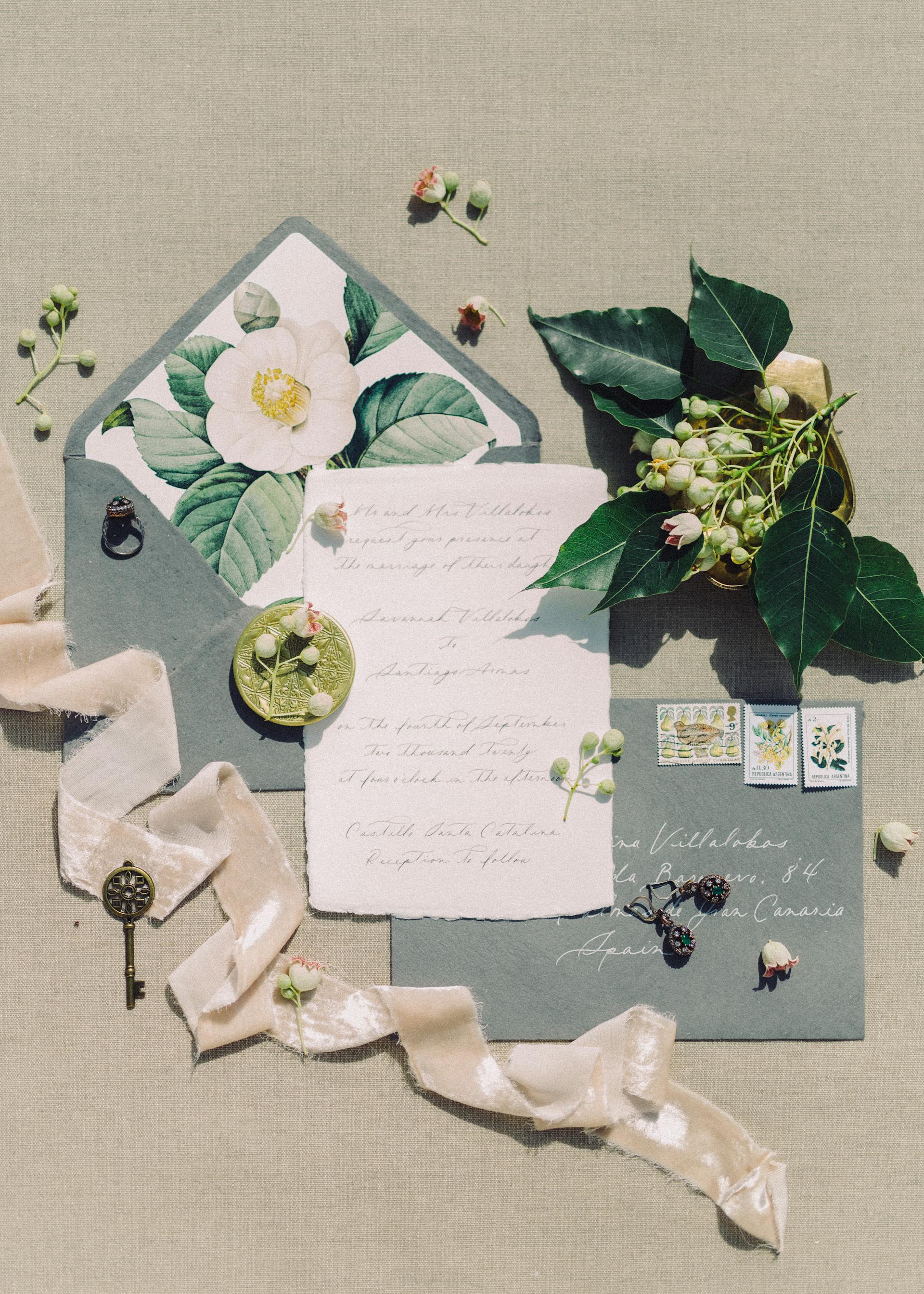 Une invitation de mariage de style vintage avec une enveloppe, un ruban, des fleurs et des timbres sur un tissu beige | Source : Pexels