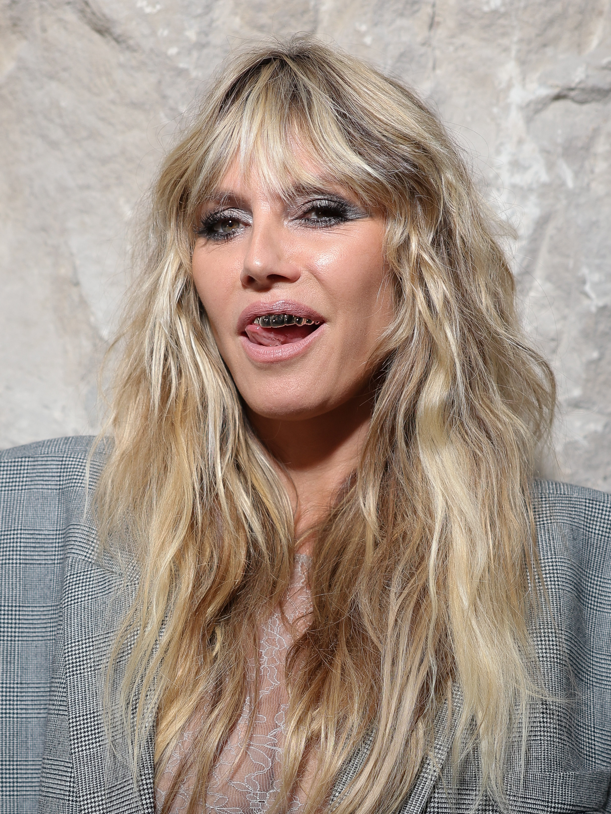 Heidi Klum a complété son look audacieux avec un maquillage smoky eye argenté saisissant et des accessoires dentaires argentées avant-gardistes, ajoutant une touche amusante et audacieuse à sa tenue.
