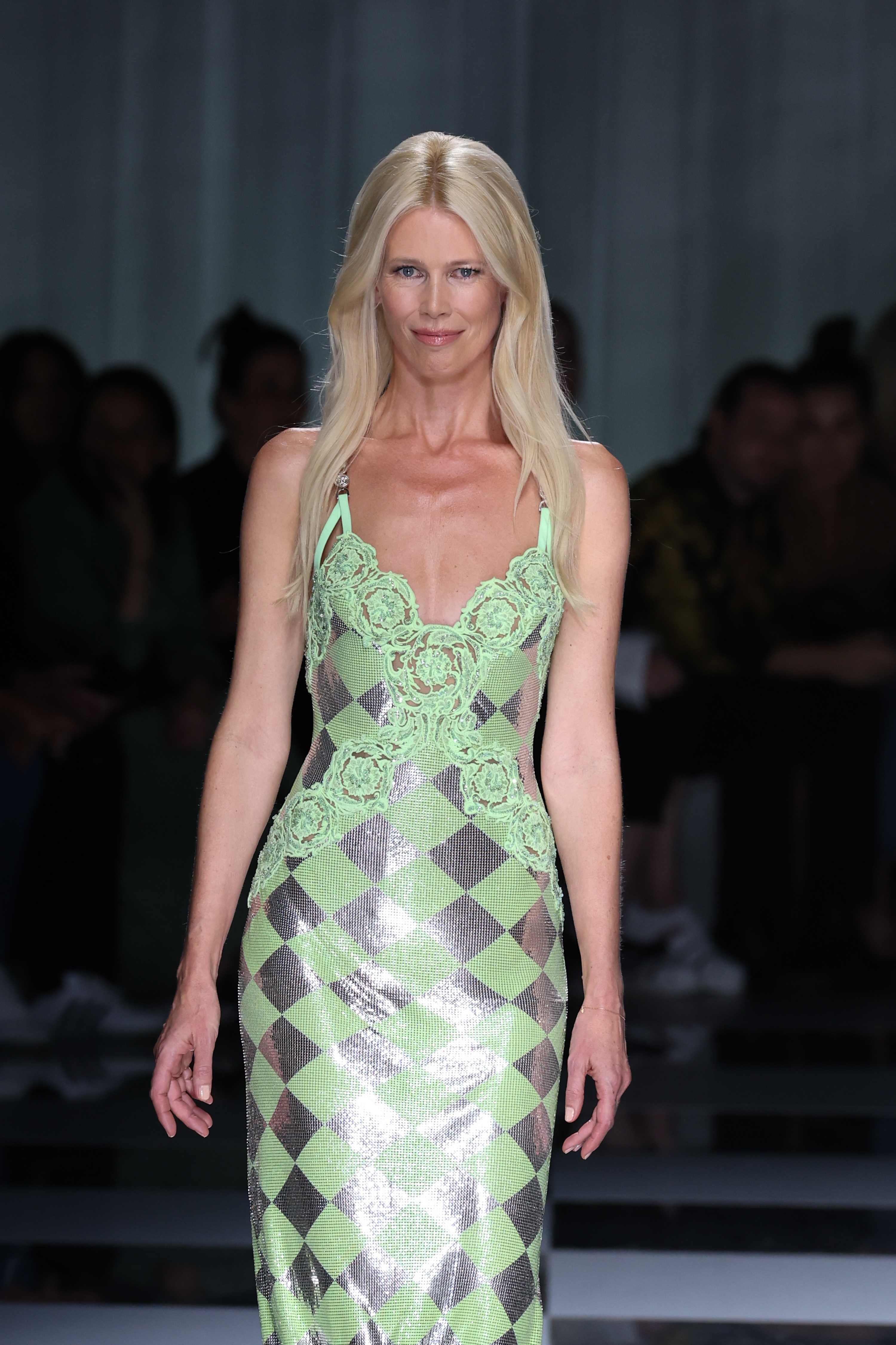 Claudia Schiffer fait un retour éblouissant sur le podium lors du défilé printemps-été de Versace à Milan, rayonnante dans une robe à carreaux vert métallique et argentée ornée de détails en dentelle. Sa démarche assurée et sa beauté intemporelle électrisent les projecteurs de la semaine de la mode.