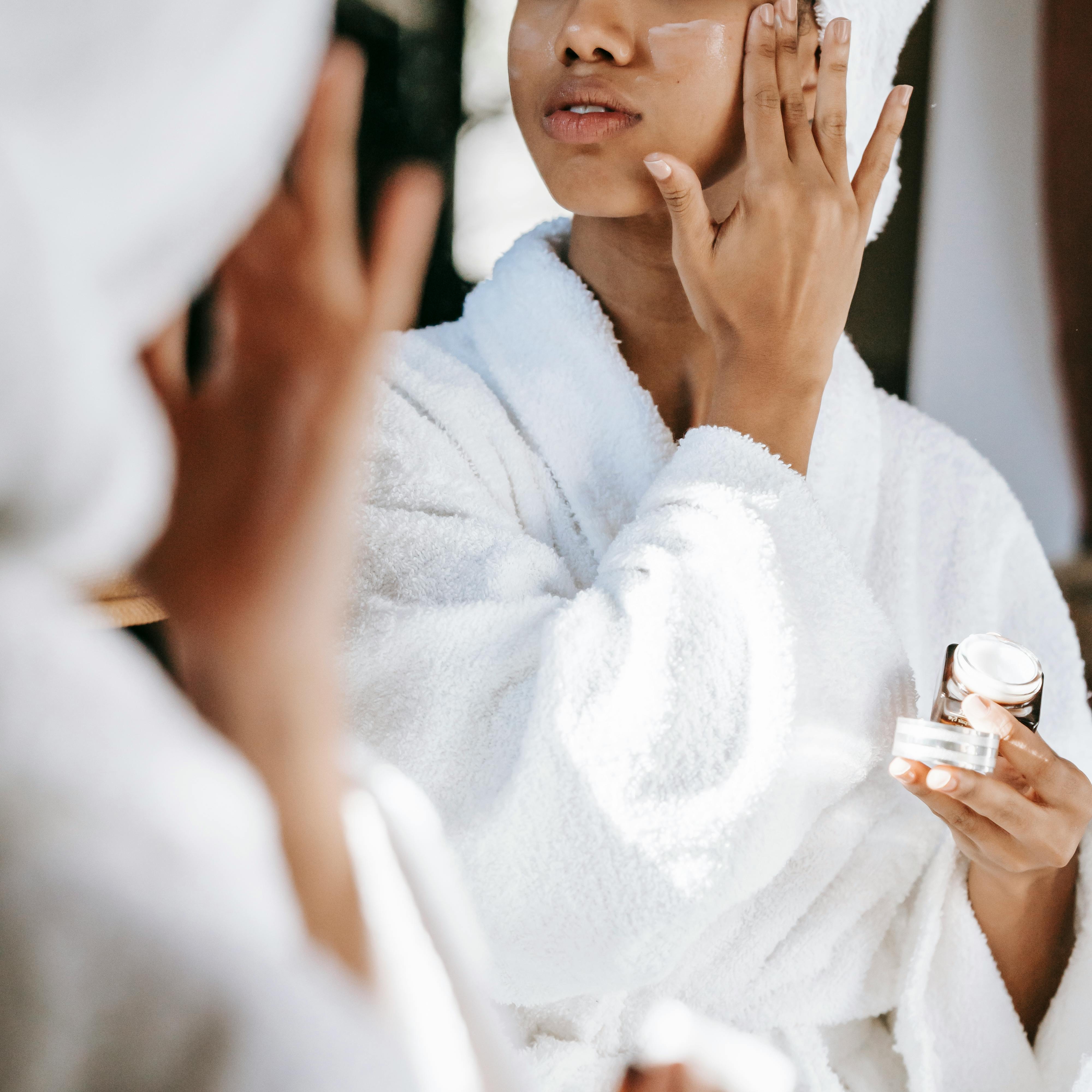 Une femme en robe de chambre, appliquant une lotion hydratante | Source : Pexels